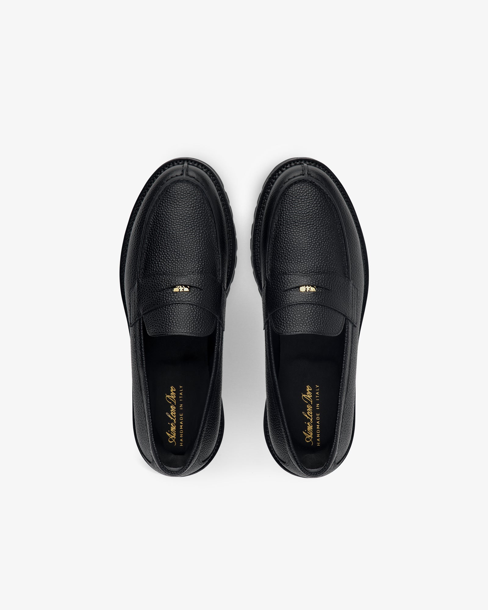 Top view of Lug Sole Queens Crest Loafer in black leather with gold insole text, shown on a light background.