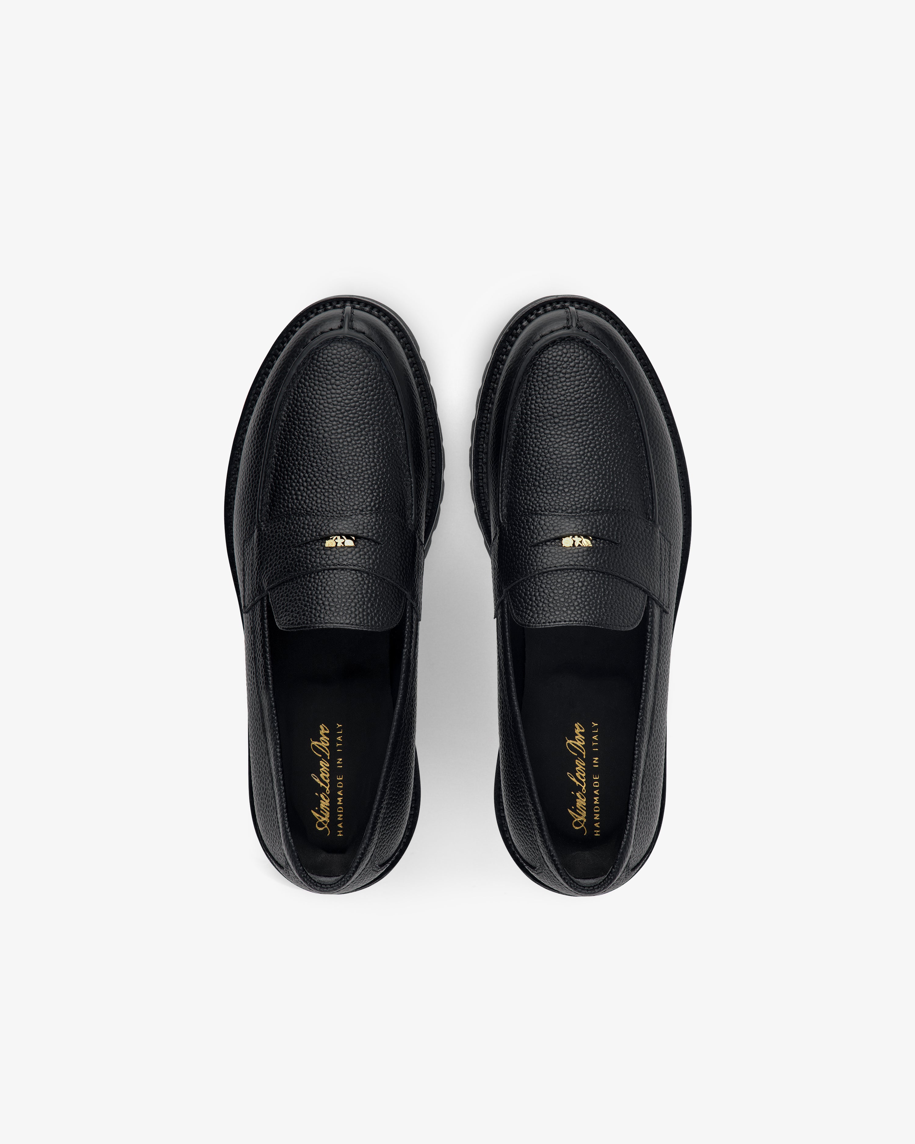 Top view of Lug Sole Queens Crest Loafer in black leather with gold insole text, shown on a light background.