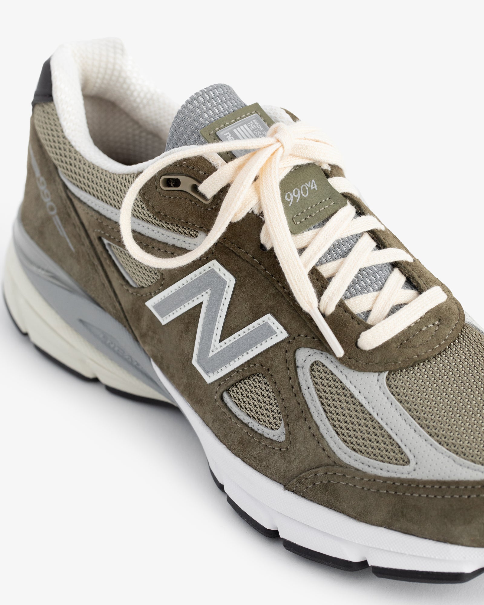 Olive green ALD / New Balance 990v4 with white laces and gray mesh accents, shown from an angle.
