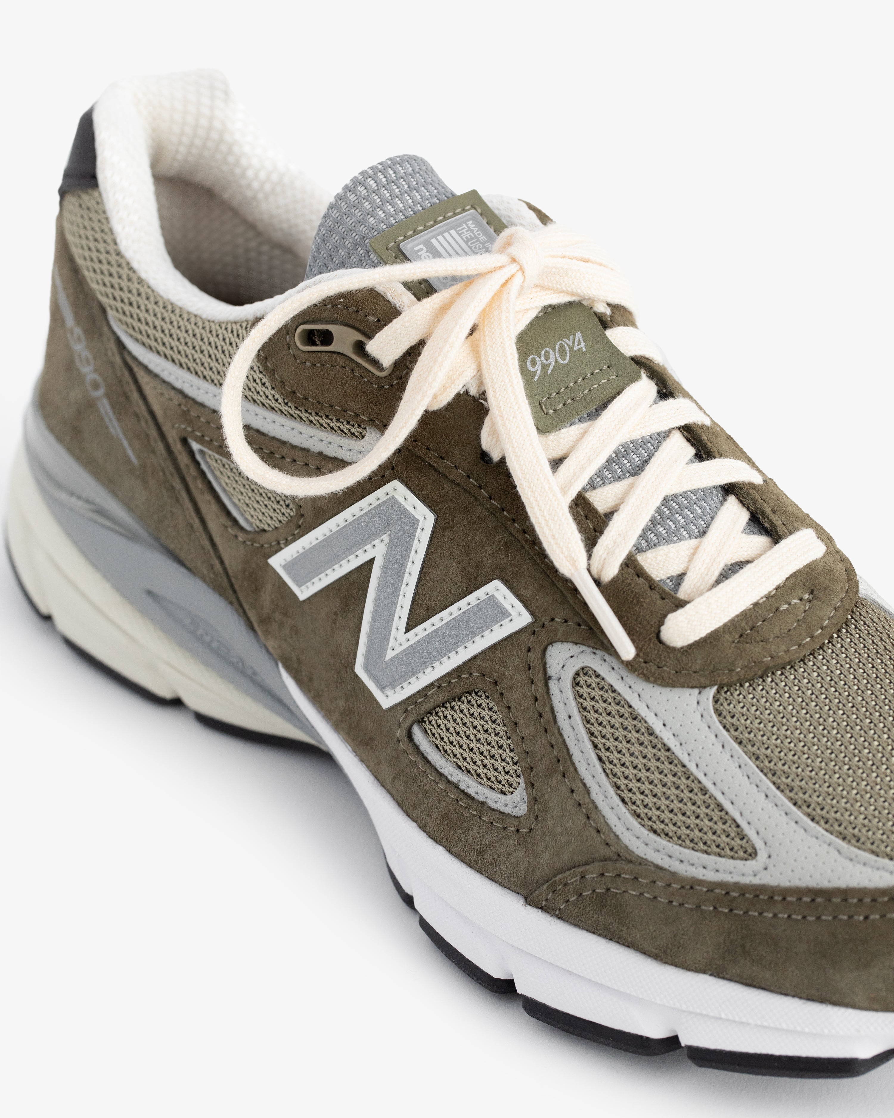Olive green ALD / New Balance 990v4 with white laces and gray mesh accents, shown from an angle.