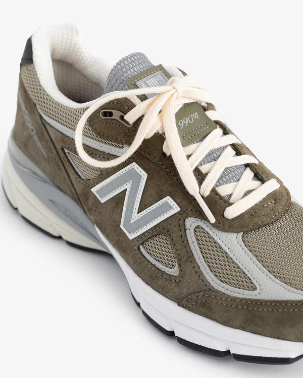 Olive green ALD / New Balance 990v4 with white laces and gray mesh accents, shown from an angle.