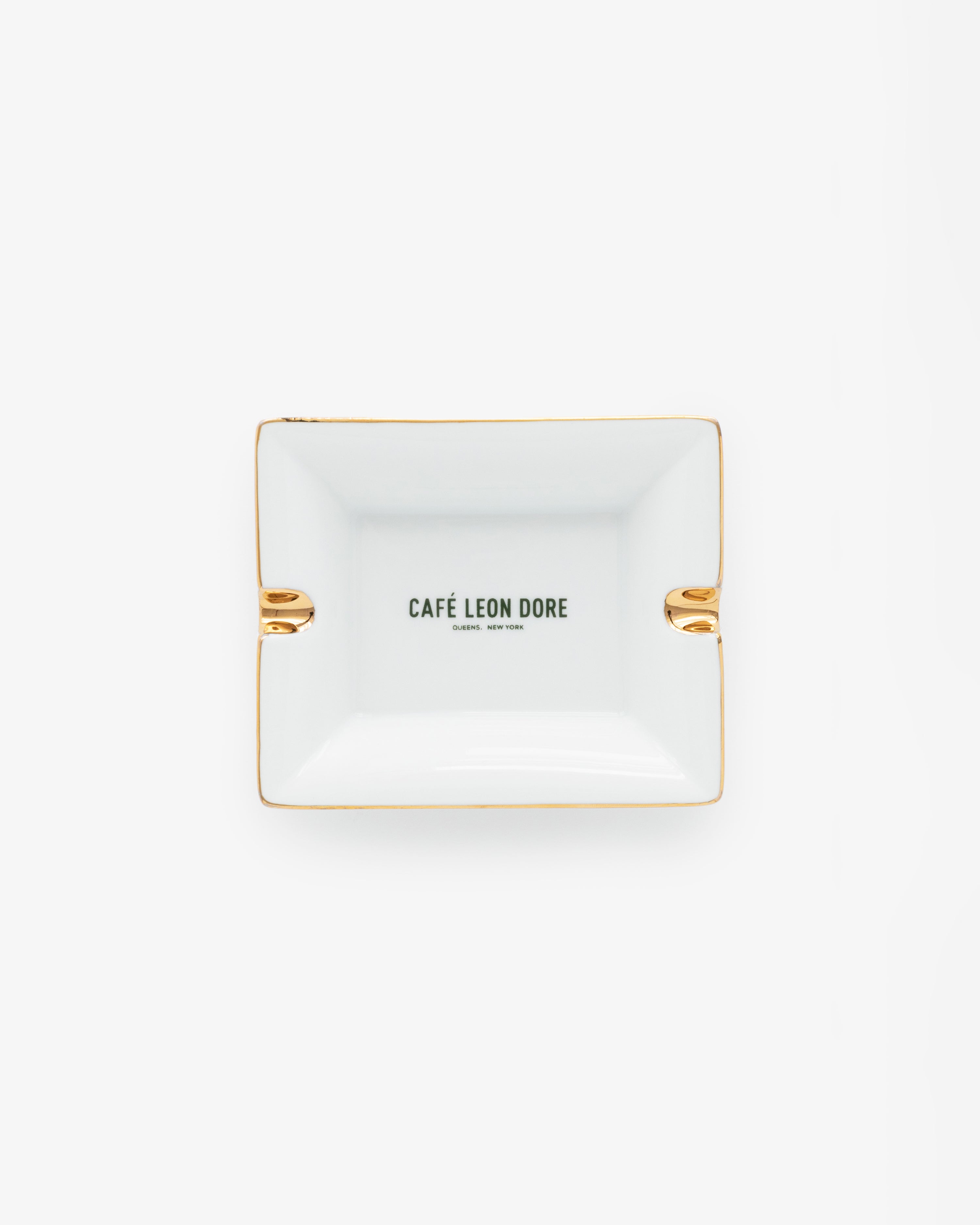 Café Leon Dore Ashtray—rectangular white with gold accents and CAFÉ LEON DORE text centered, on a plain background.