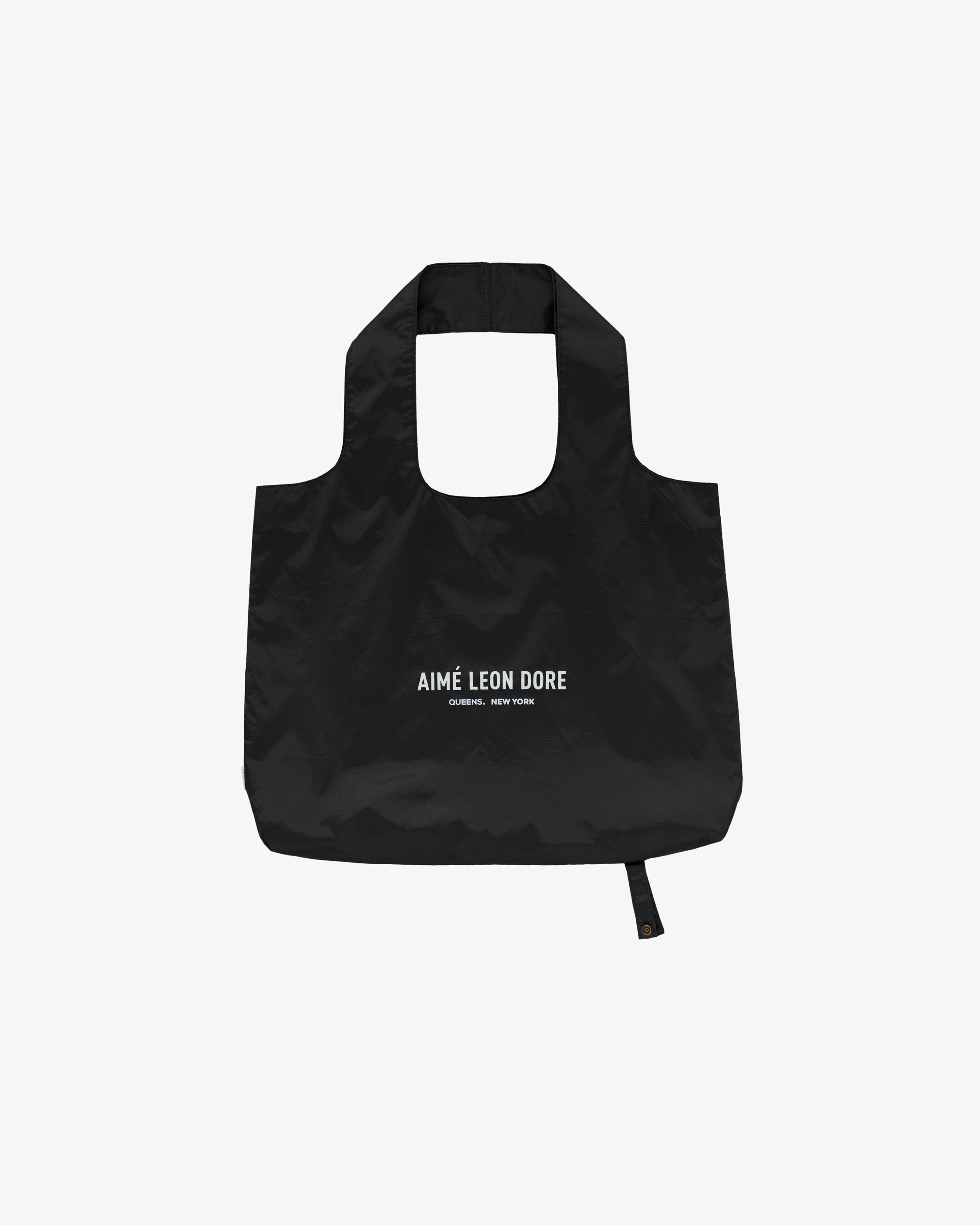 Packable Logo Tote: black reusable bag with AIMÉ LEON DORE and QUEENS, NEW YORK printed in white on front.
