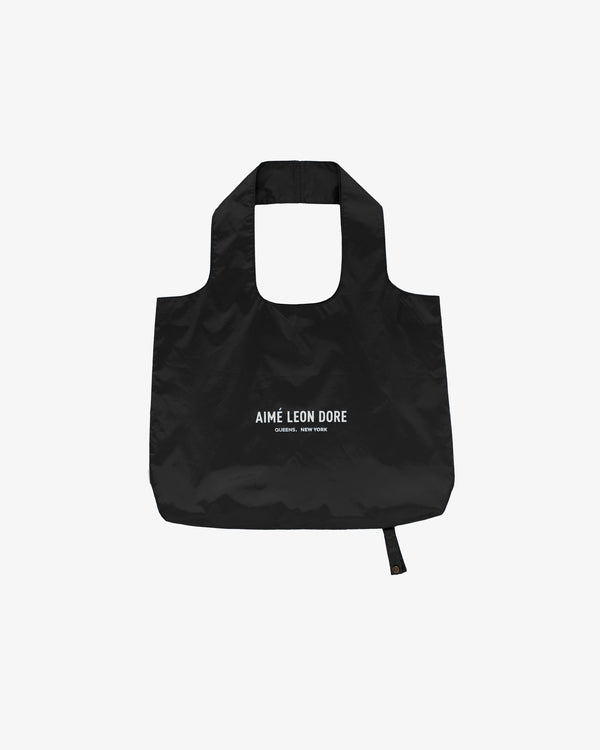 Packable Logo Tote: black reusable bag with AIMÉ LEON DORE and QUEENS, NEW YORK printed in white on front.