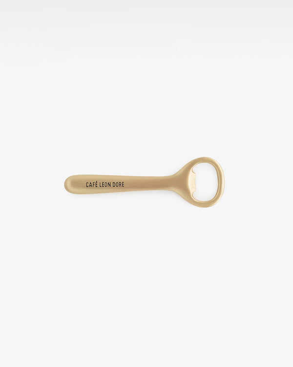 Café Leon Dore Bottle Opener in gold with logo on handle, displayed against a plain white background.