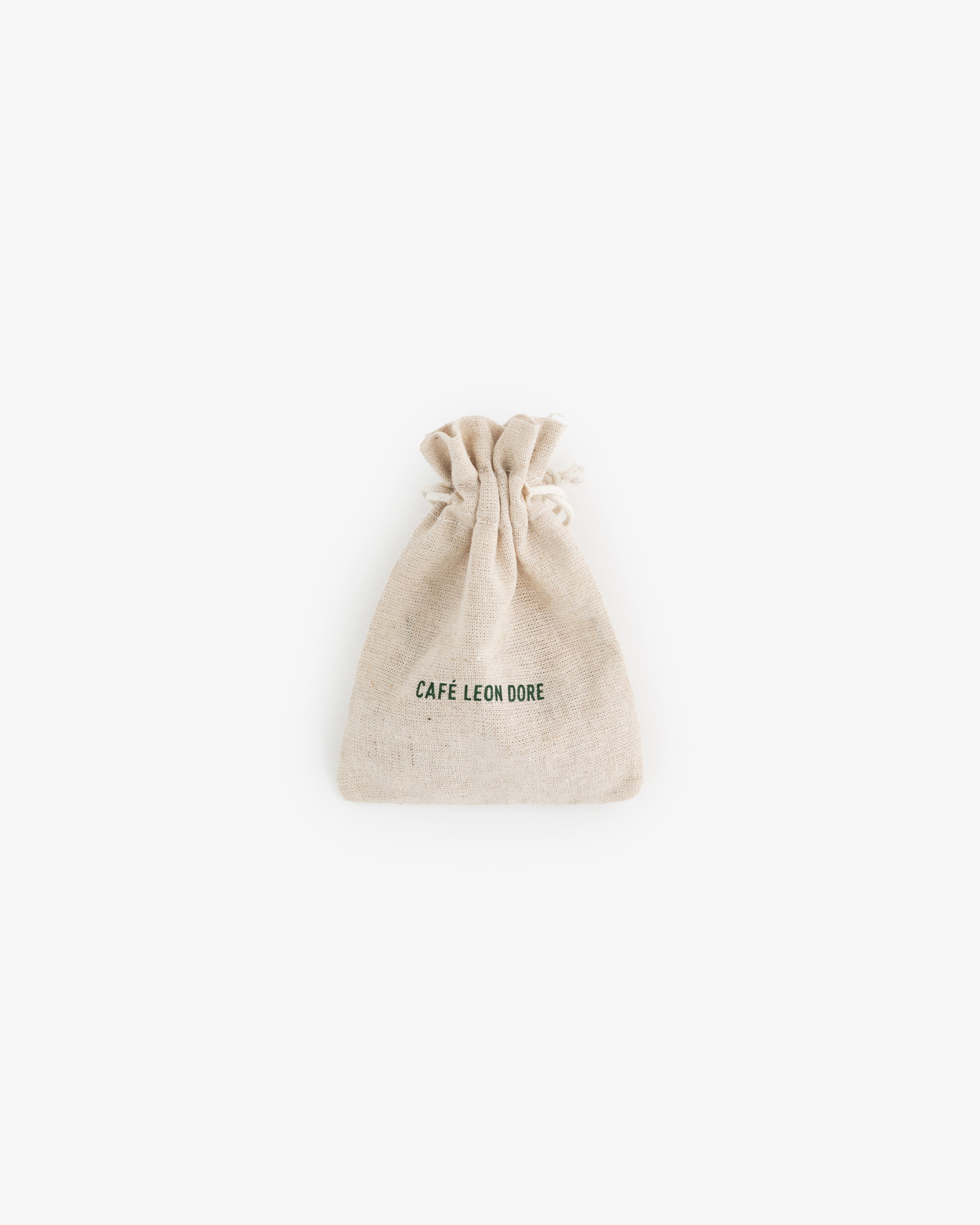 A small beige drawstring pouch for Café Leon Dore Komboloi, with branding on the front, centered on a white background.