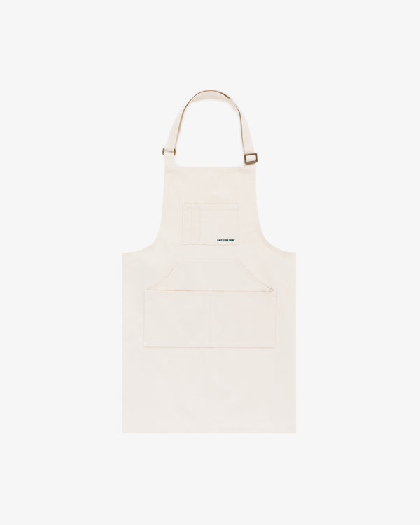 The Café Leon Dore Apron in plain beige features a front pocket and adjustable neck strap, shown on a white background.