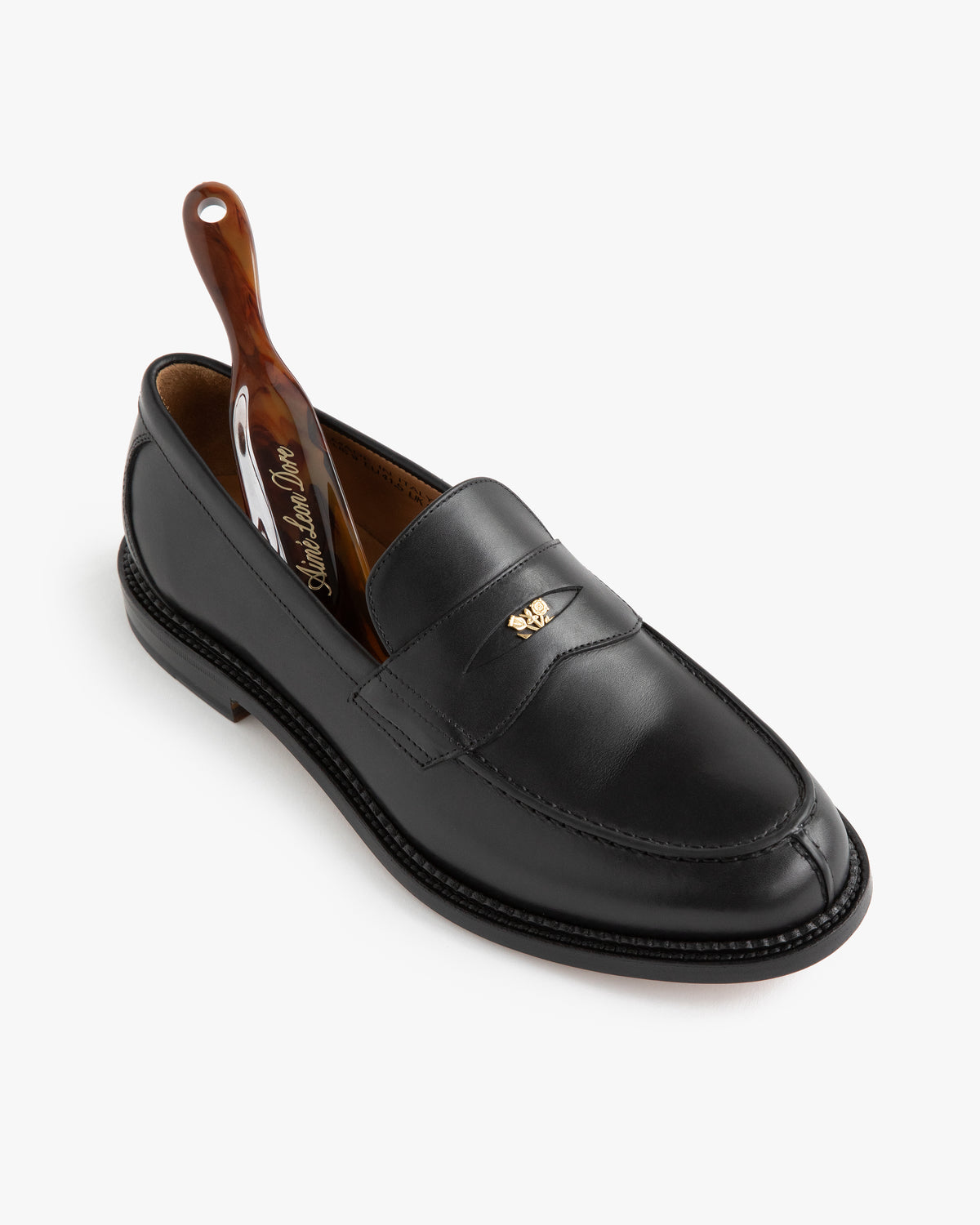 Queens Crest Loafer in black leather with a brown shoehorn, shown on a white background.