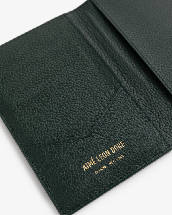 Open dark green leather passport holder with AIMÉ LEON DORE QUEENS, NEW YORK stamped in gold inside.