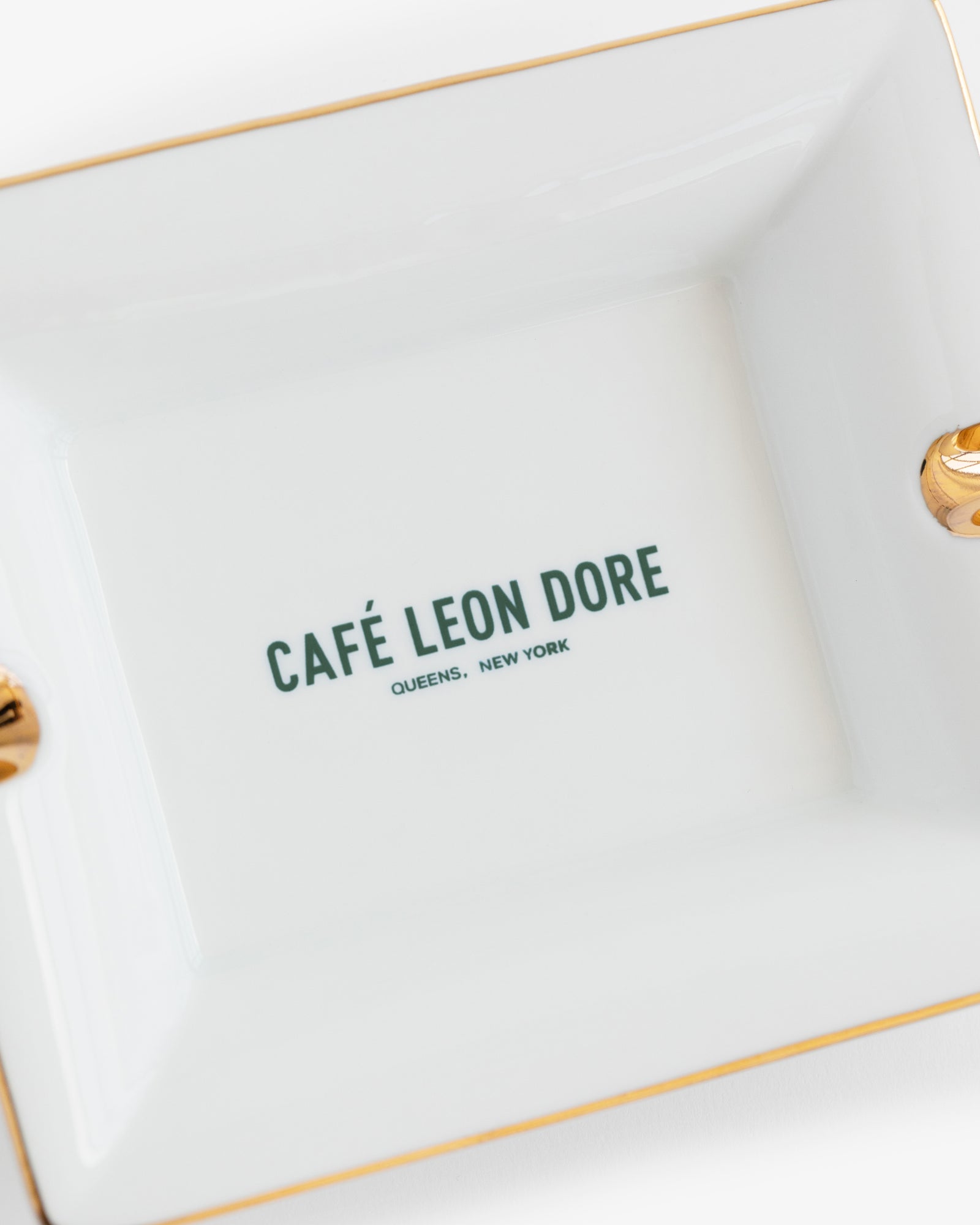 Café Leon Dore Ashtray: White porcelain with gold trim, green "CAFÉ LEON DORE QUEENS, NEW YORK" at center.