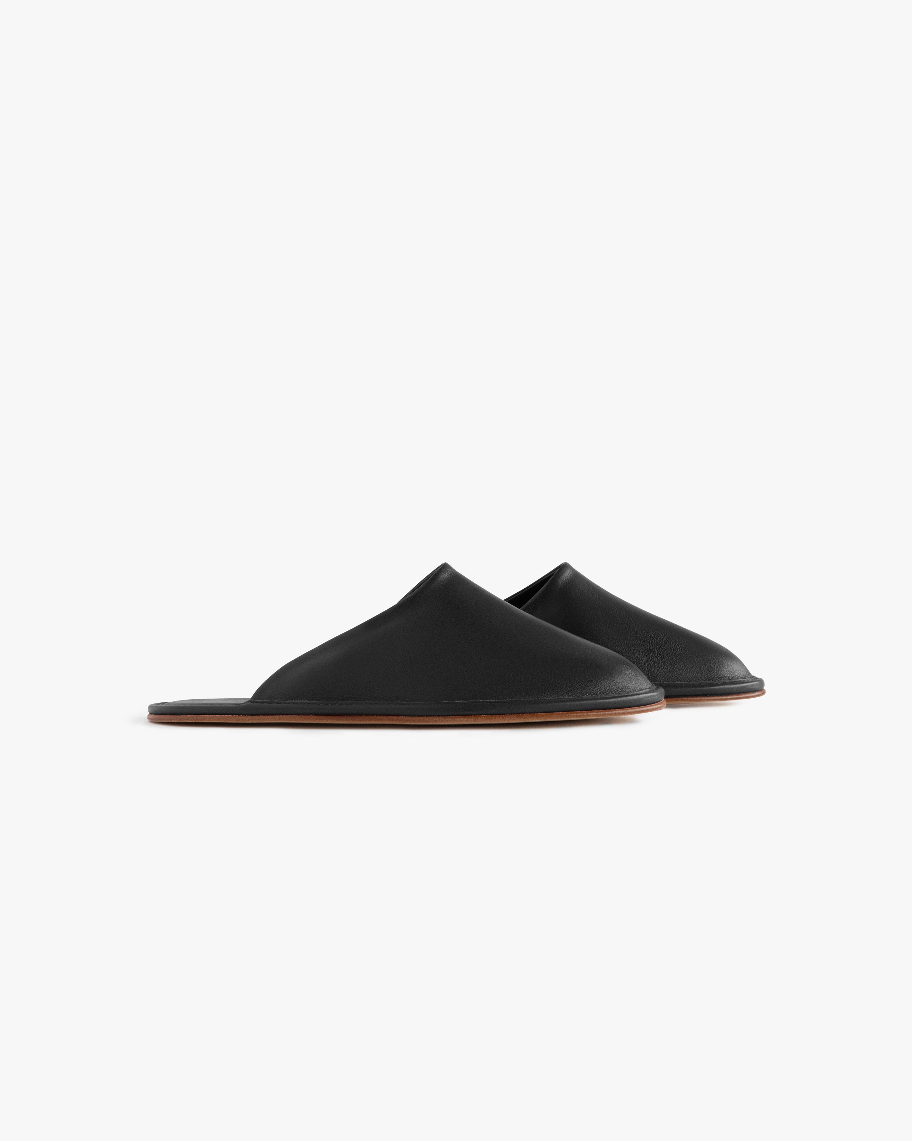Leather Travel Slipper: black leather slip-ons with flat brown soles, shown on a white background.