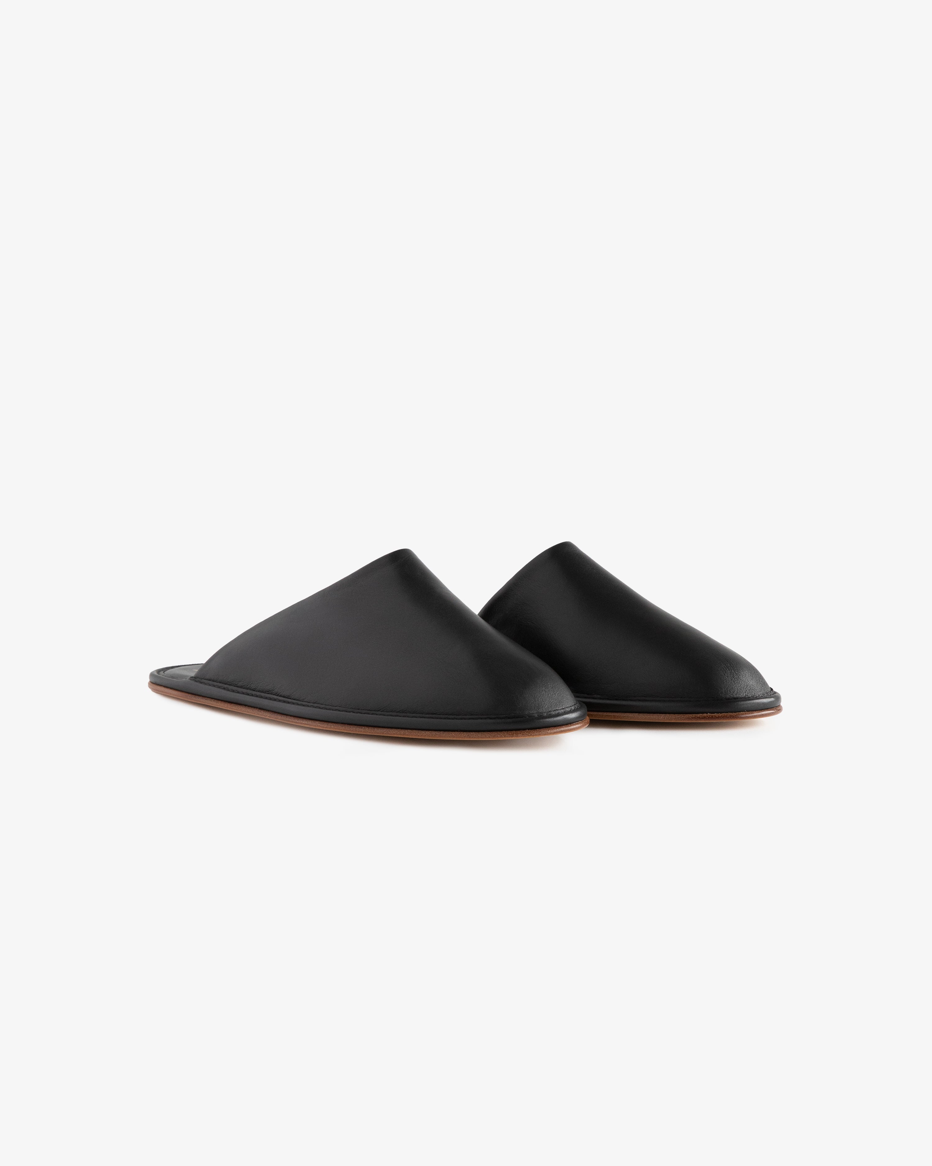 A pair of Leather Travel Slippers in black leather with brown soles on a white background.