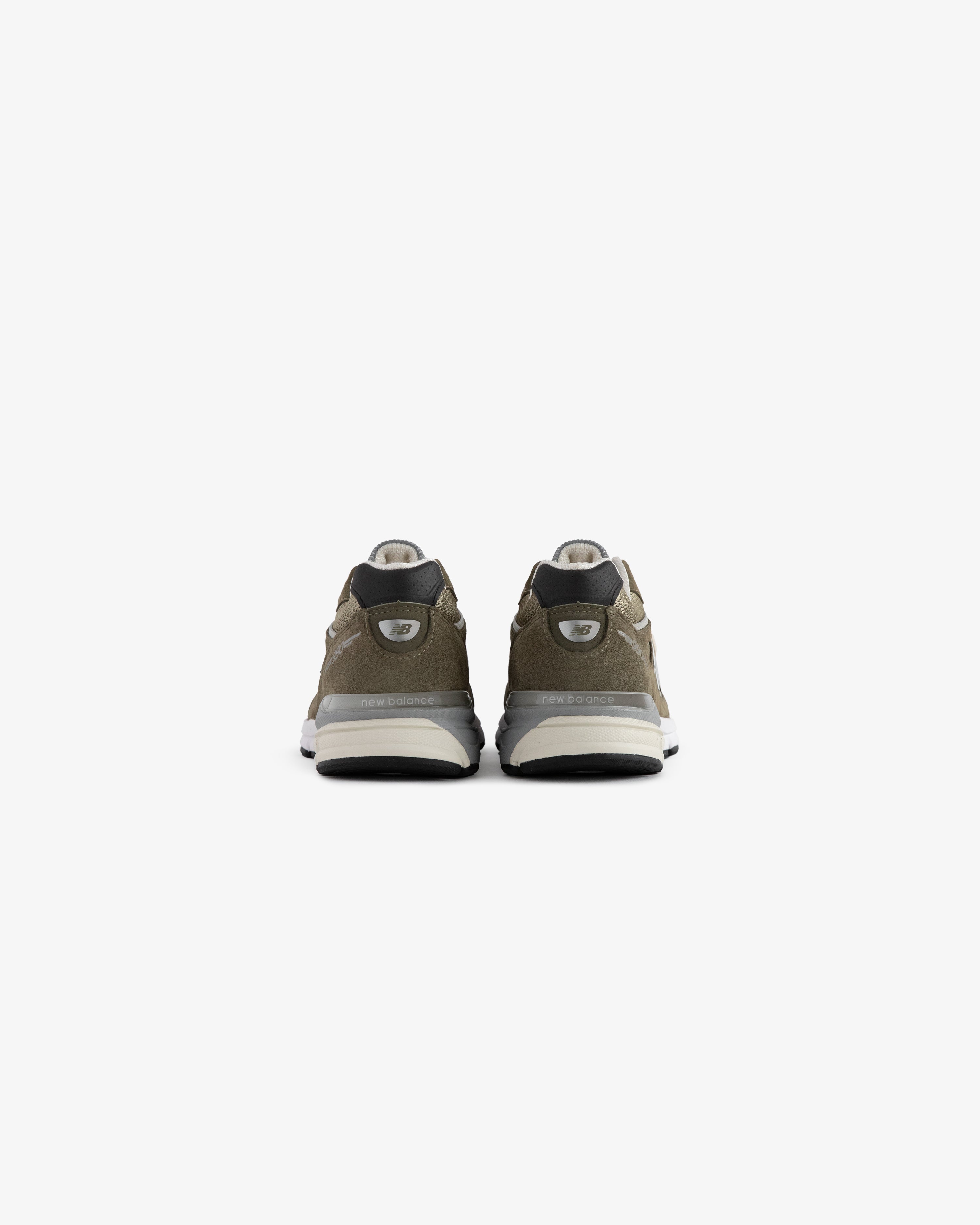 ALD / New Balance 990v4 olive green sneakers with white soles and black accents, shown from the back on white.
