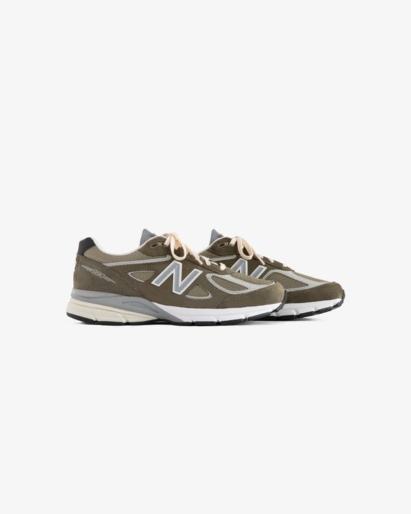 A pair of olive green ALD / New Balance 990v4 sneakers with white soles and beige laces on a white background.