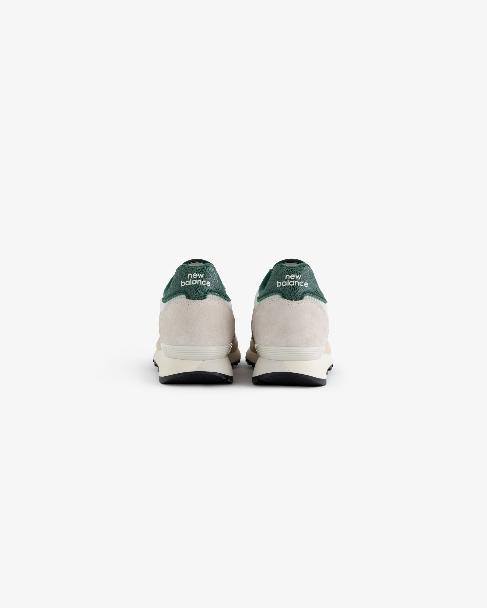 A pair of ALD / New Balance 475 sneakers viewed from the back, featuring green heel tabs and white midsoles.