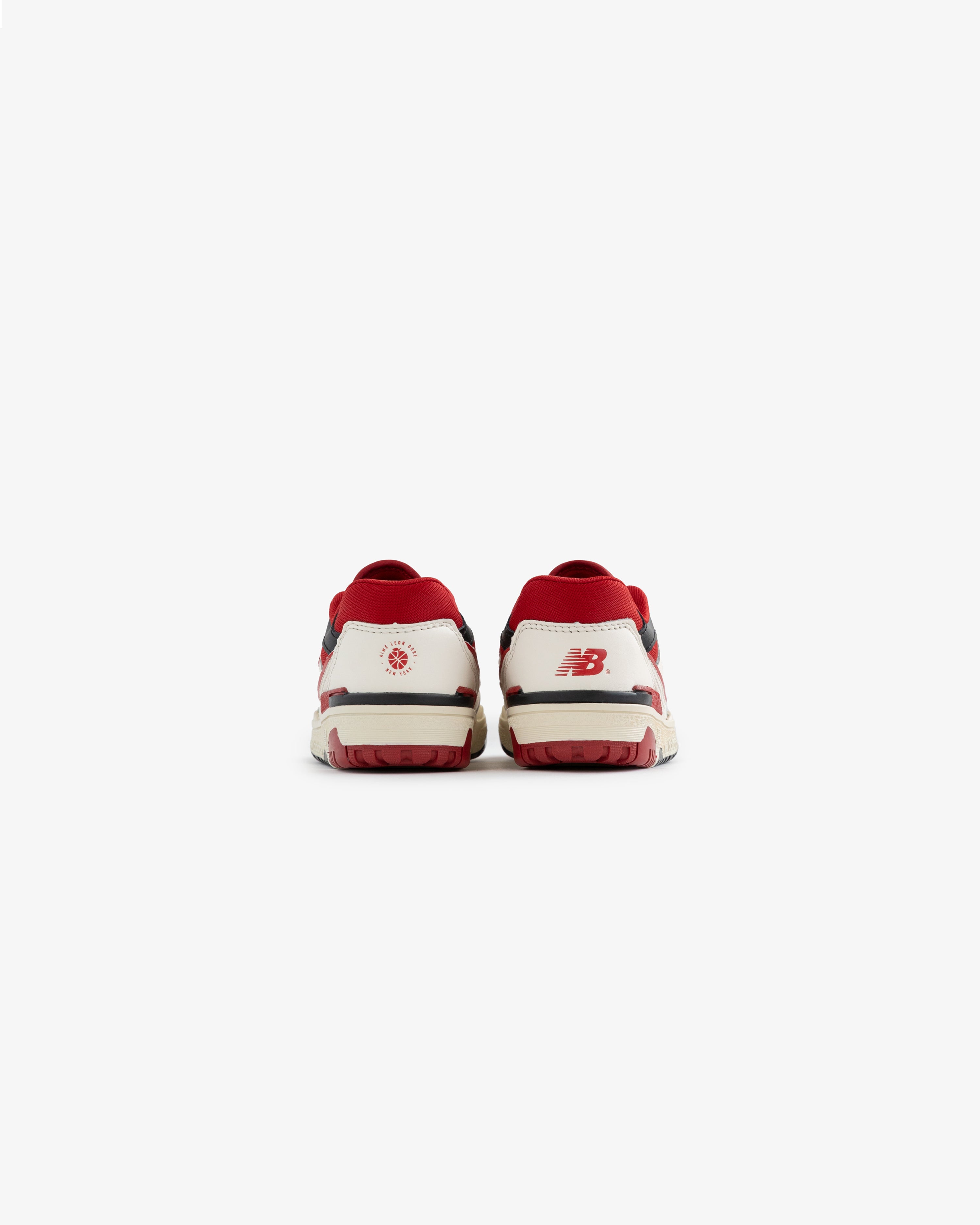 Back view of ALD / NB P550 Basketball Oxfords - Little Kids in white and red with heel logos on a plain white background.