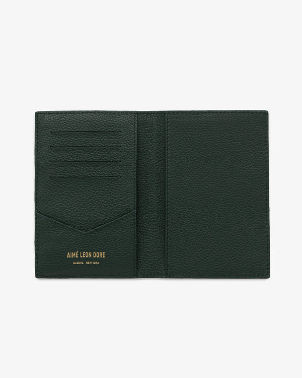 Dark green leather passport holder with card slots and gold AIMÉ LEON DORE QUEENS, NEW YORK text at the bottom.