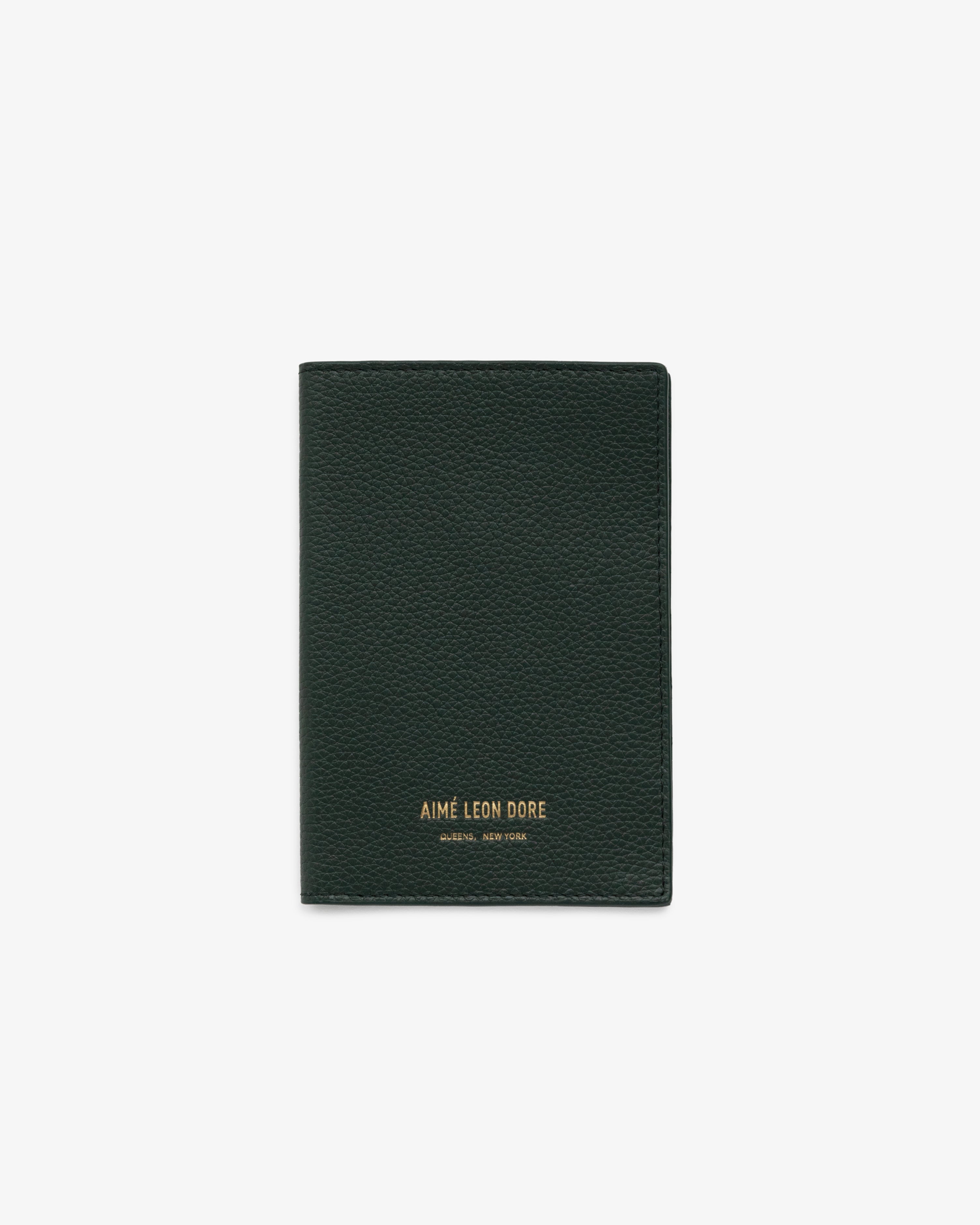 Dark green leather passport holder with gold AIMÉ LEON DORE branding at the bottom center, on a white background.
