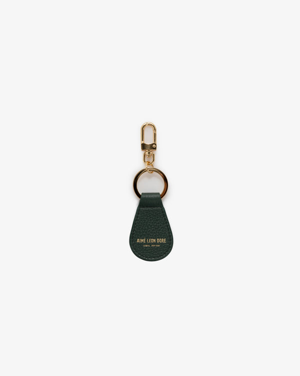 The Leather Key Fob is dark green leather with gold hardware and "Aime Leon Dore" embossed in gold at the bottom.