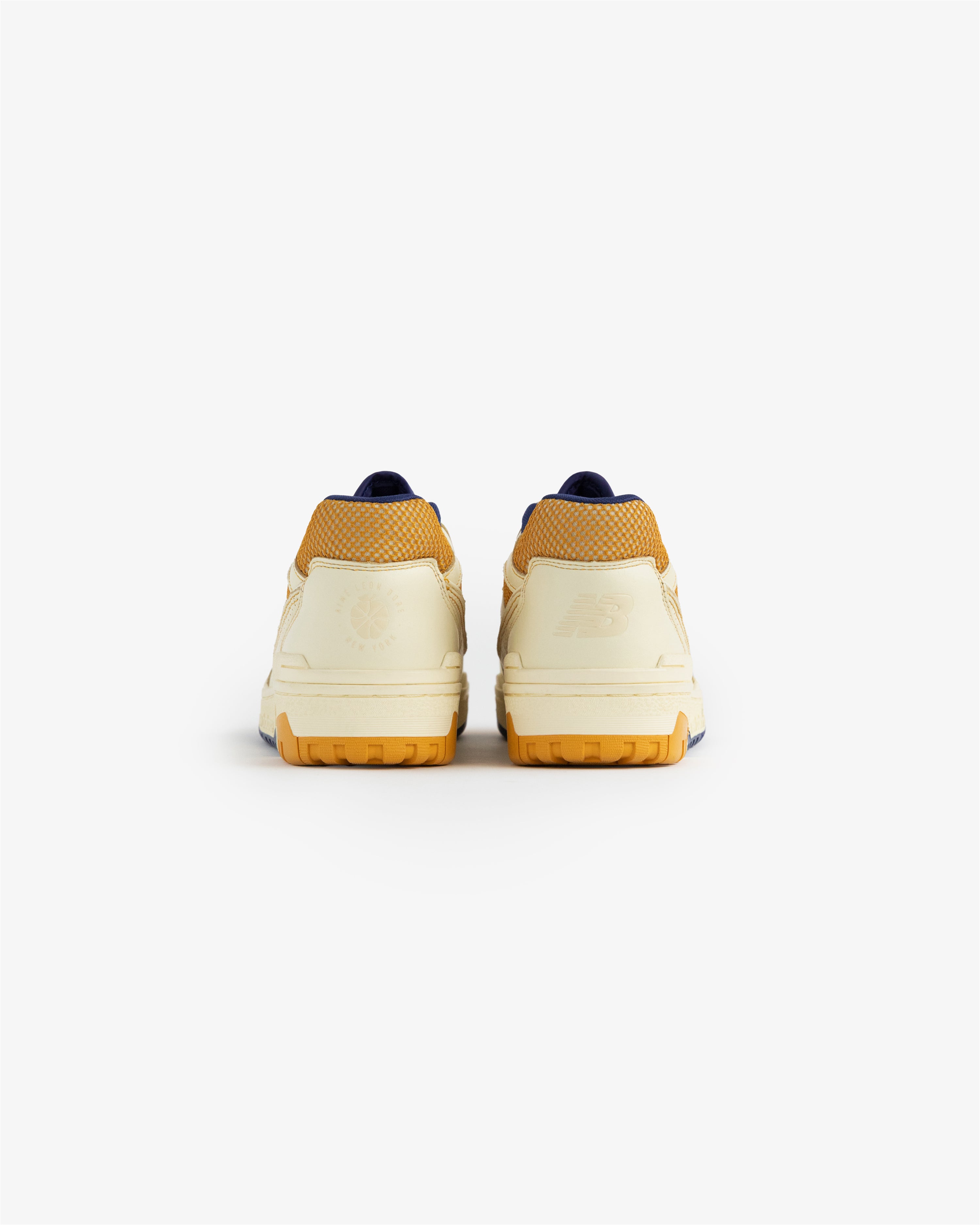 Rear view of ALD / NB P550 Basketball Oxfords in cream and yellow, rubber soles, on a plain white background.