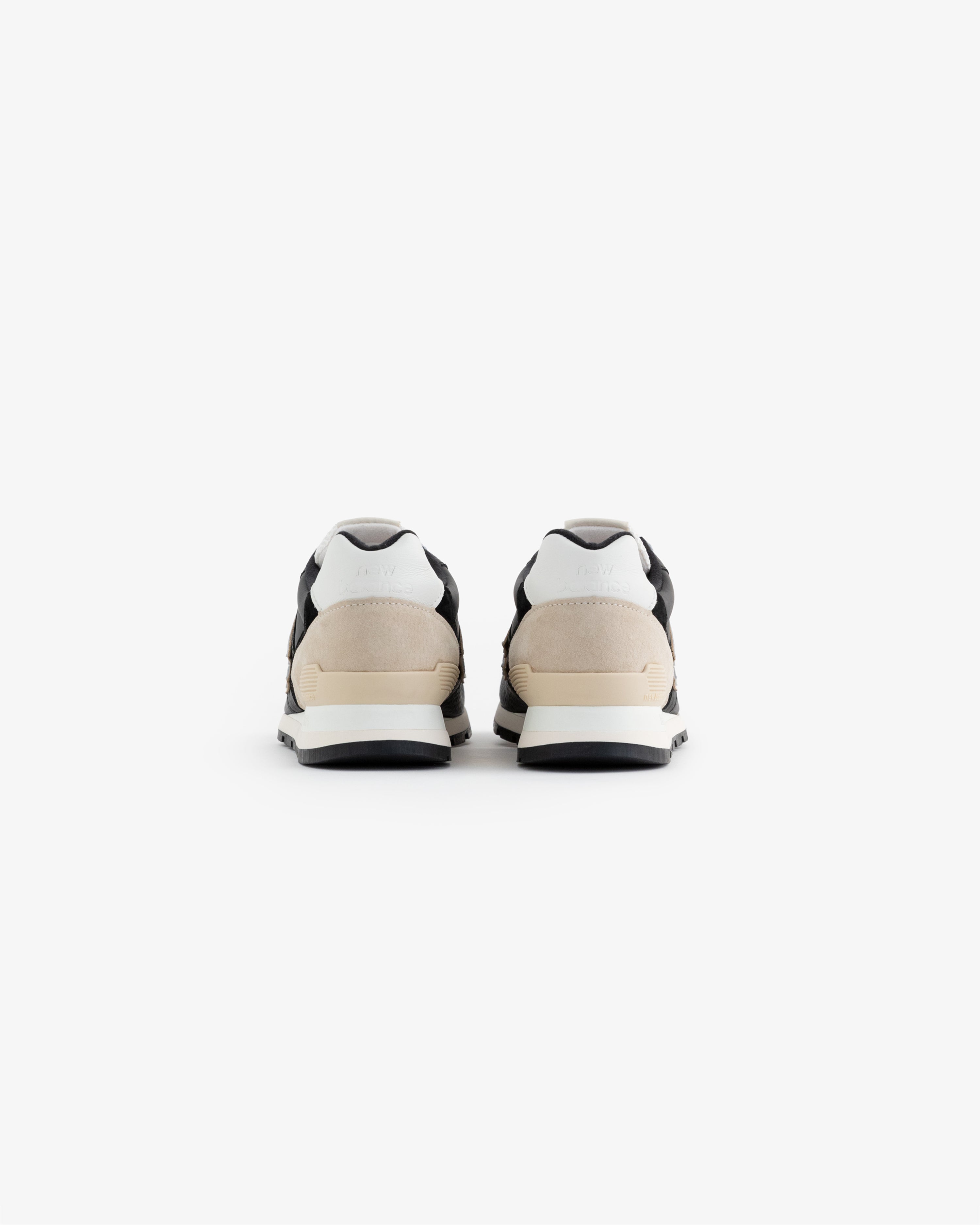A pair of ALD / NB Made in USA 996 sneakers in black, white, and beige shown from the back on a white background.
