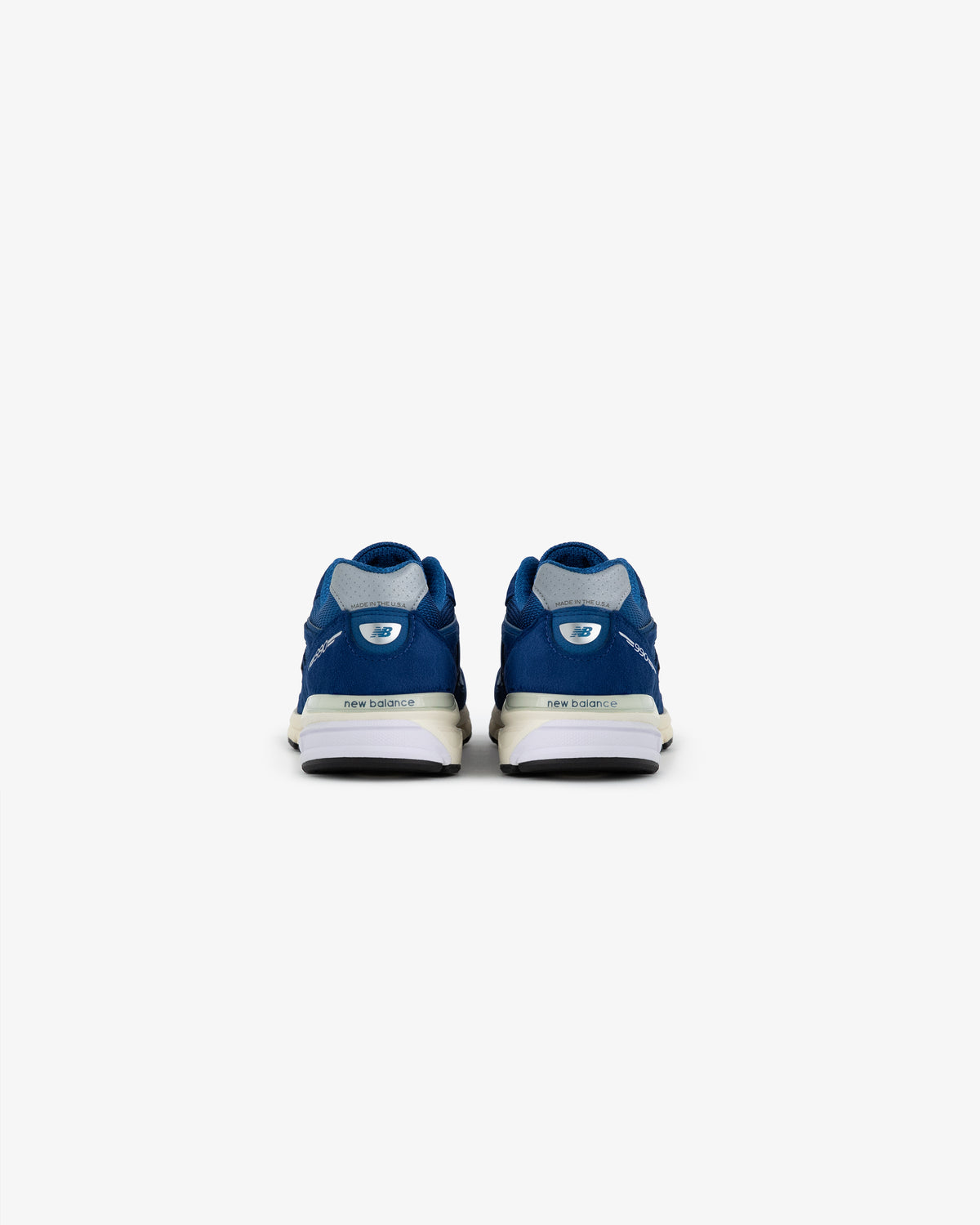 ALD / NB Made in USA 990v4 blue sneakers seen from the back on a plain white background.