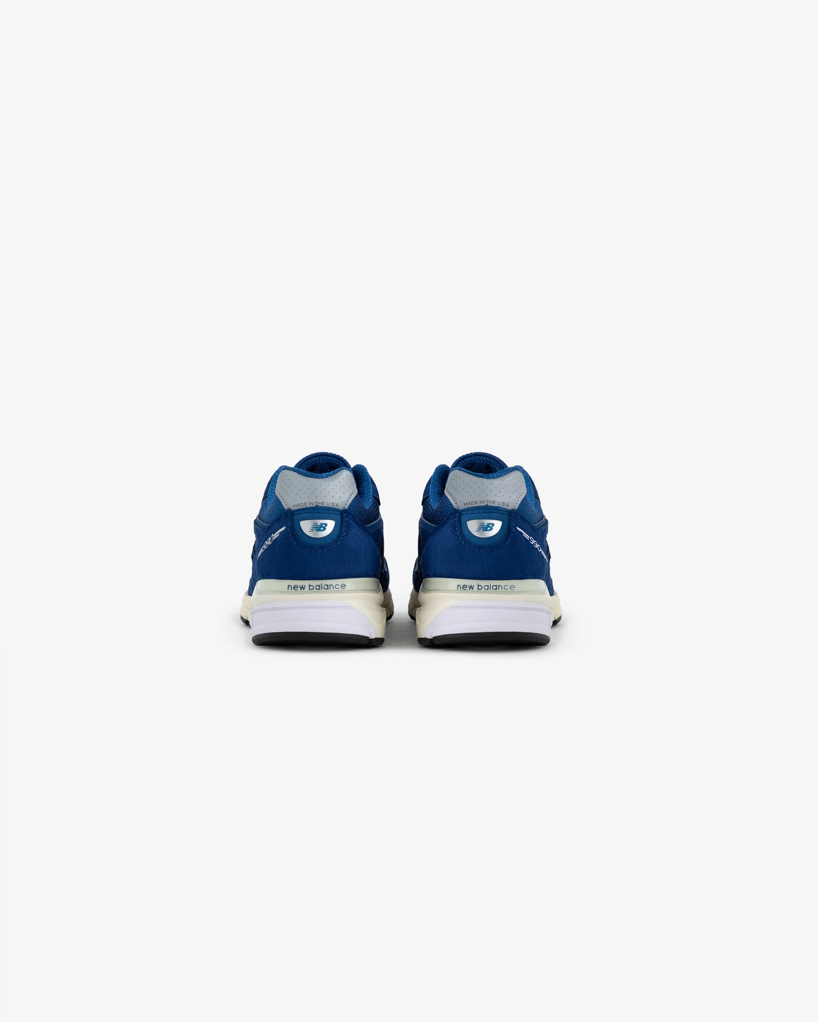 ALD / NB Made in USA 990v4 blue sneakers seen from the back on a plain white background.
