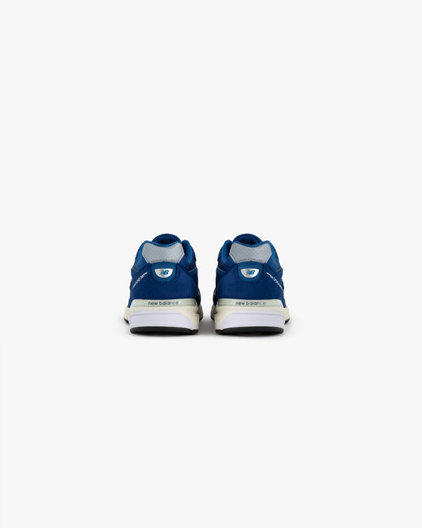 ALD / NB Made in USA 990v4 blue sneakers seen from the back on a plain white background.