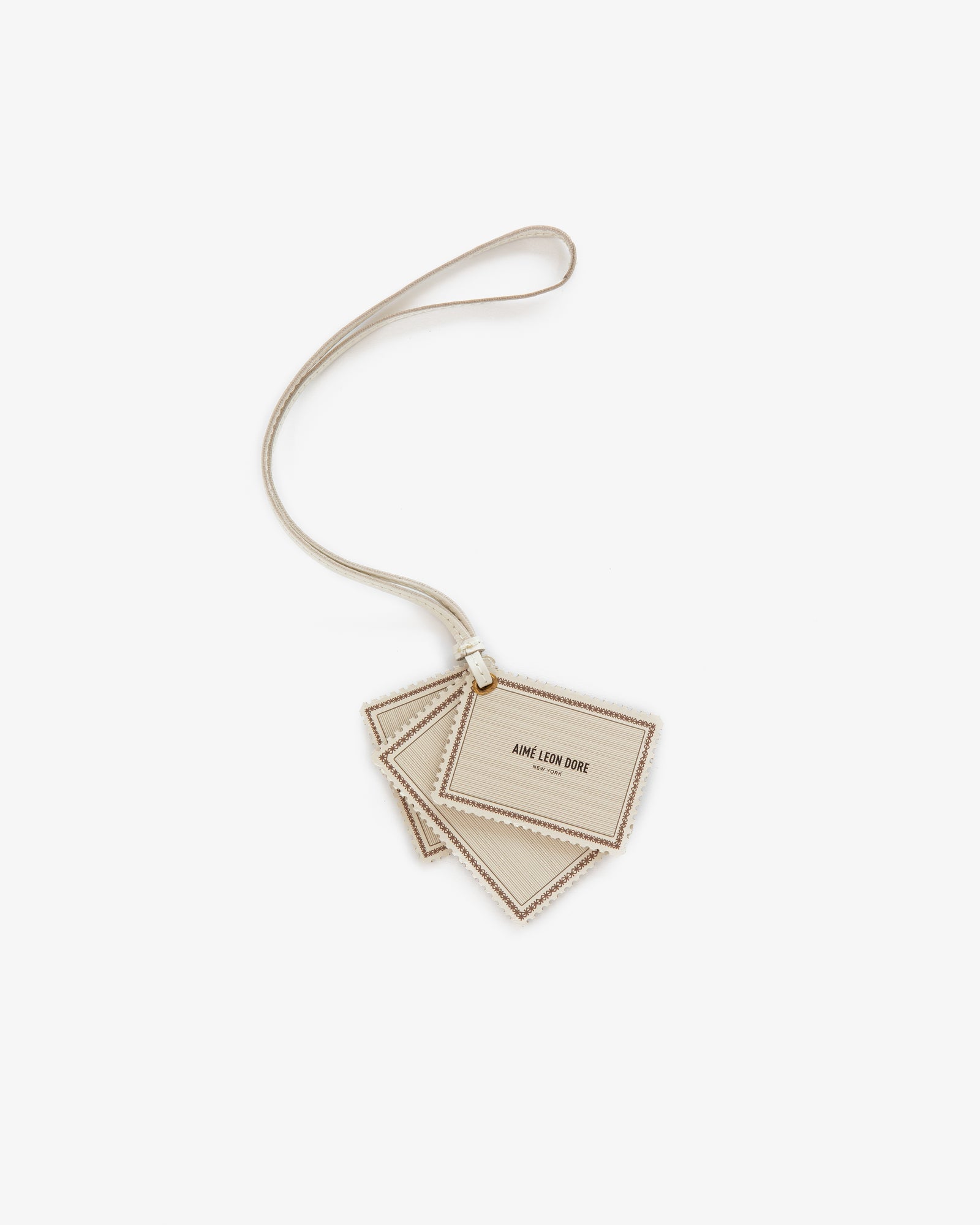 Beige Leather Traveler Charm with AIME LEON DORE text, attached to a matching strap, on a white background.