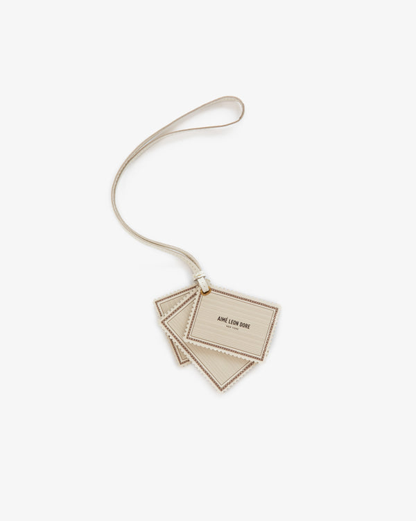 Beige Leather Traveler Charm with AIME LEON DORE text, attached to a matching strap, on a white background.