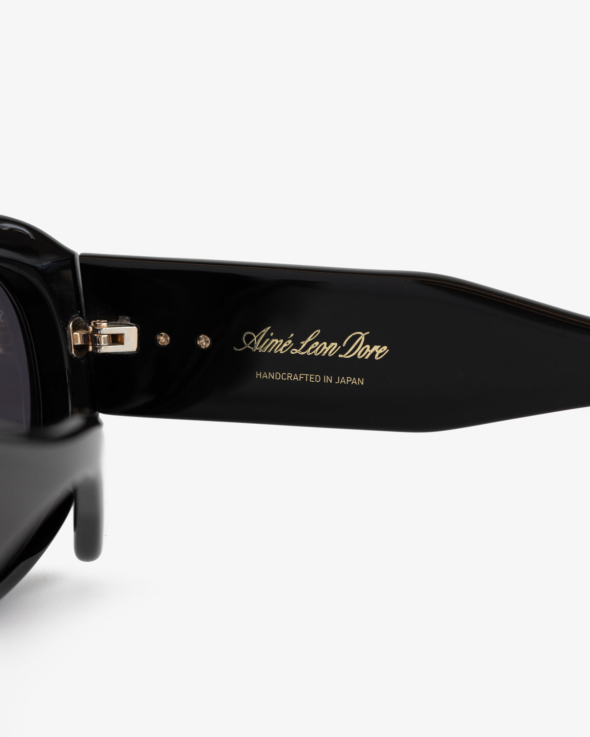 Close-up of Jackie O Sunglasses' black arm with gold Aimé Leon Dore and Handcrafted in Japan text inside.