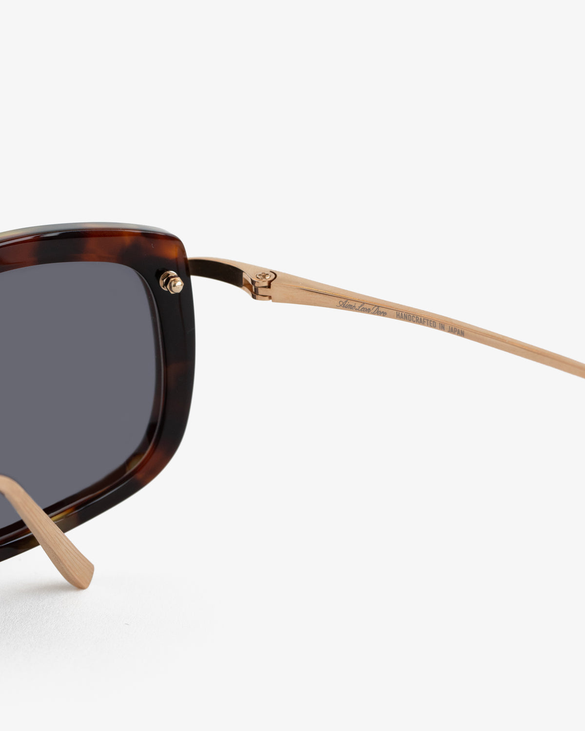 Close-up of Ace Sunglasses with a tortoiseshell frame and gold metal arms against a white background.