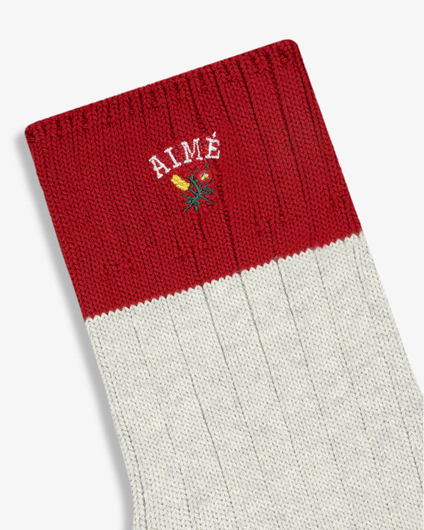 The Crest Varsity Sock is a red and white ribbed sock with AIMÉ and a small flower embroidered near the top.