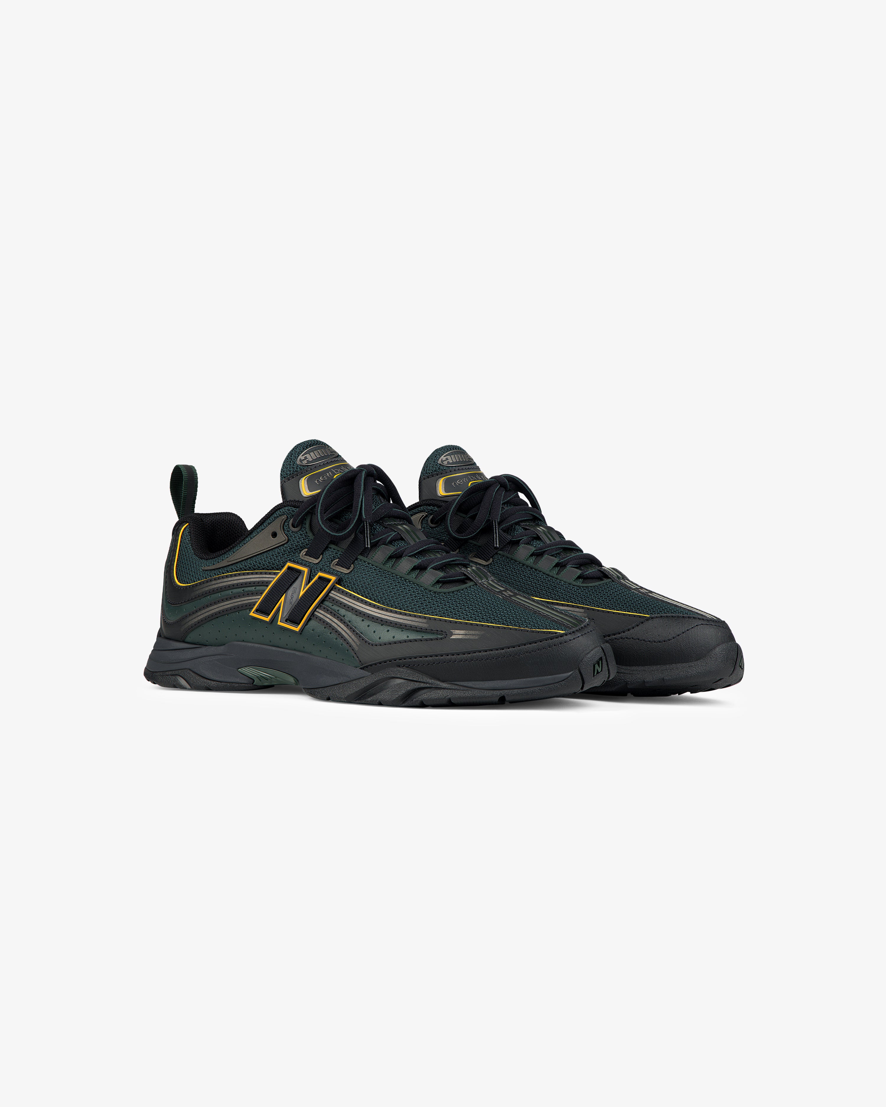 A pair of ALD / New Balance RC56 sneakers in dark green and black with yellow accents, on a white background.