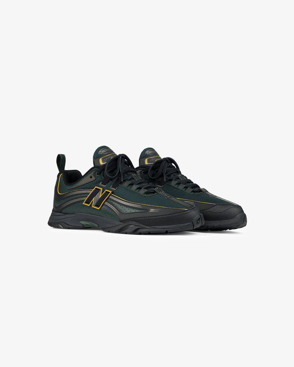 A pair of ALD / New Balance RC56 sneakers in dark green and black with yellow accents, on a white background.