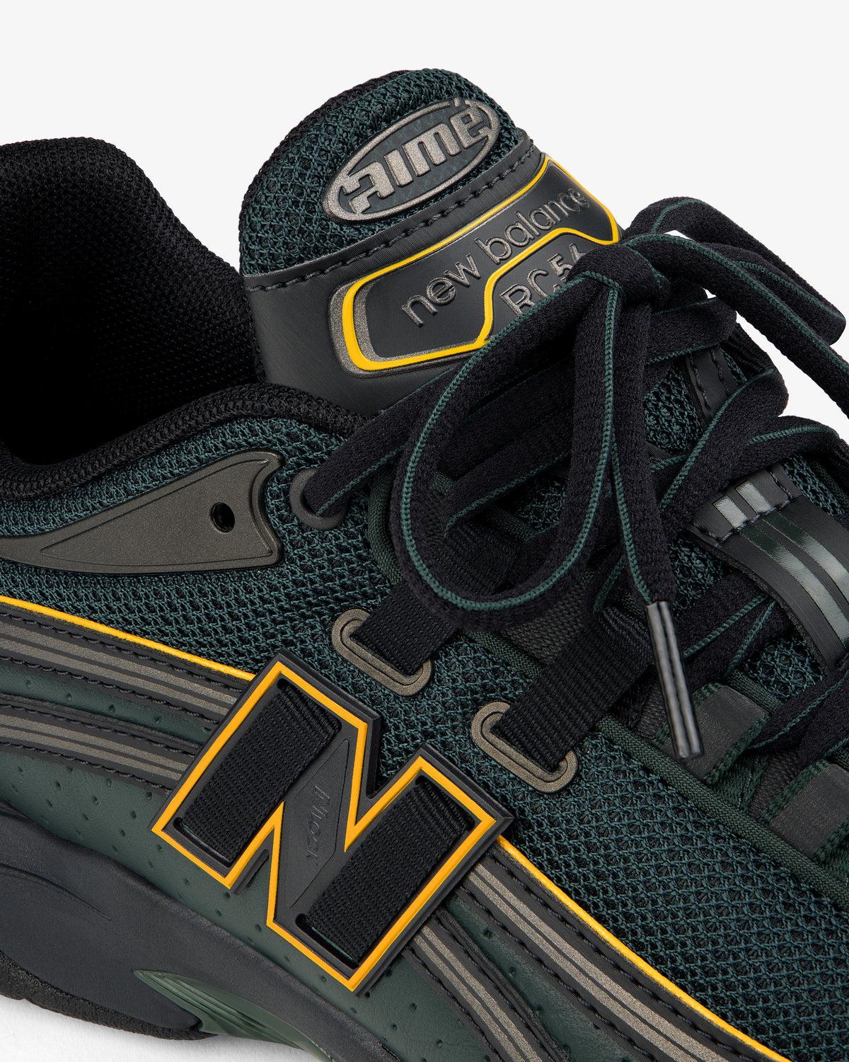 Close-up of a dark green ALD / New Balance RC56 with yellow accents and black laces on a white background.