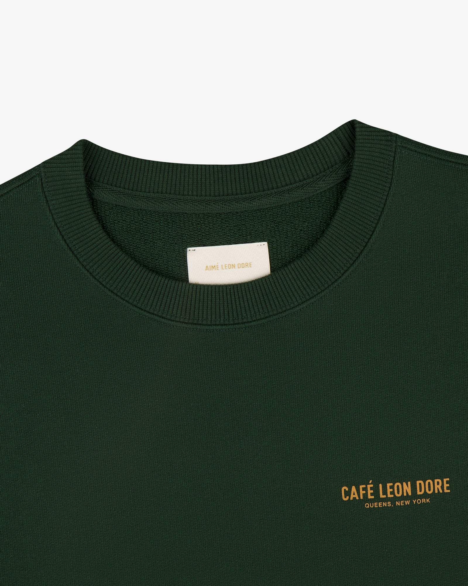 Café Leon Dore Crewneck Sweatshirt in dark green with yellow "CAFÉ LEON DORE QUEENS, NEW YORK" chest print.