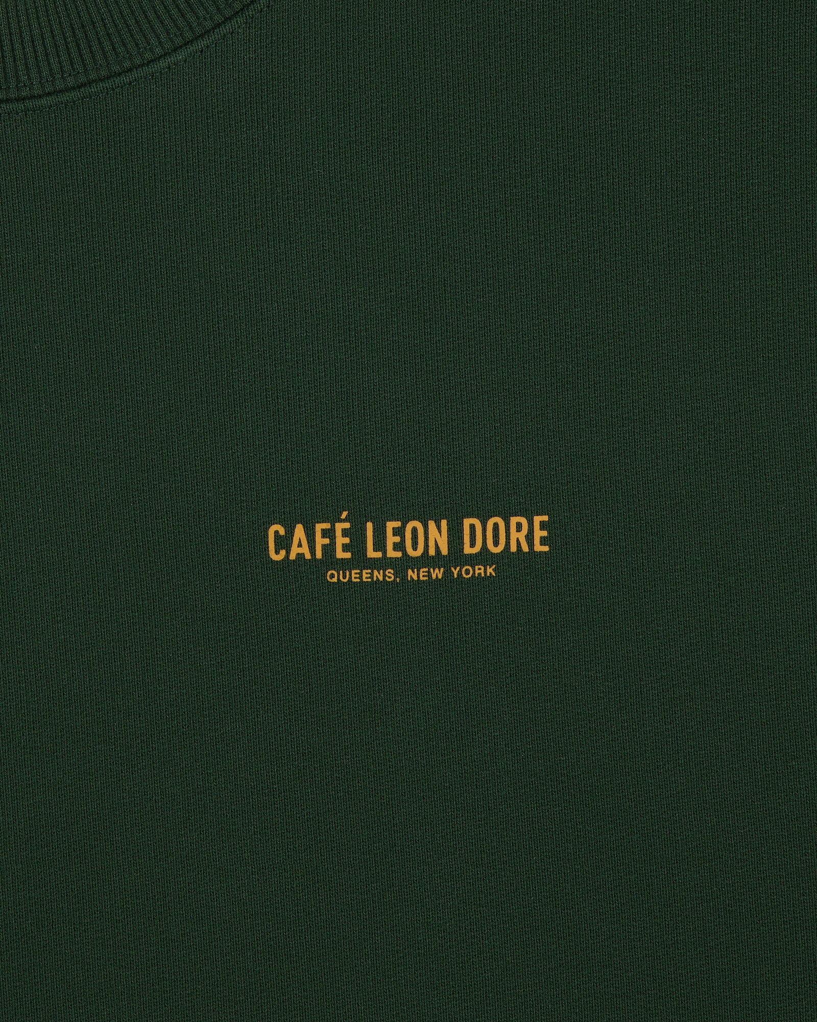 Dark green Café Leon Dore Crewneck Sweatshirt with yellow "CAFÉ LEON DORE QUEENS, NEW YORK" text at center.