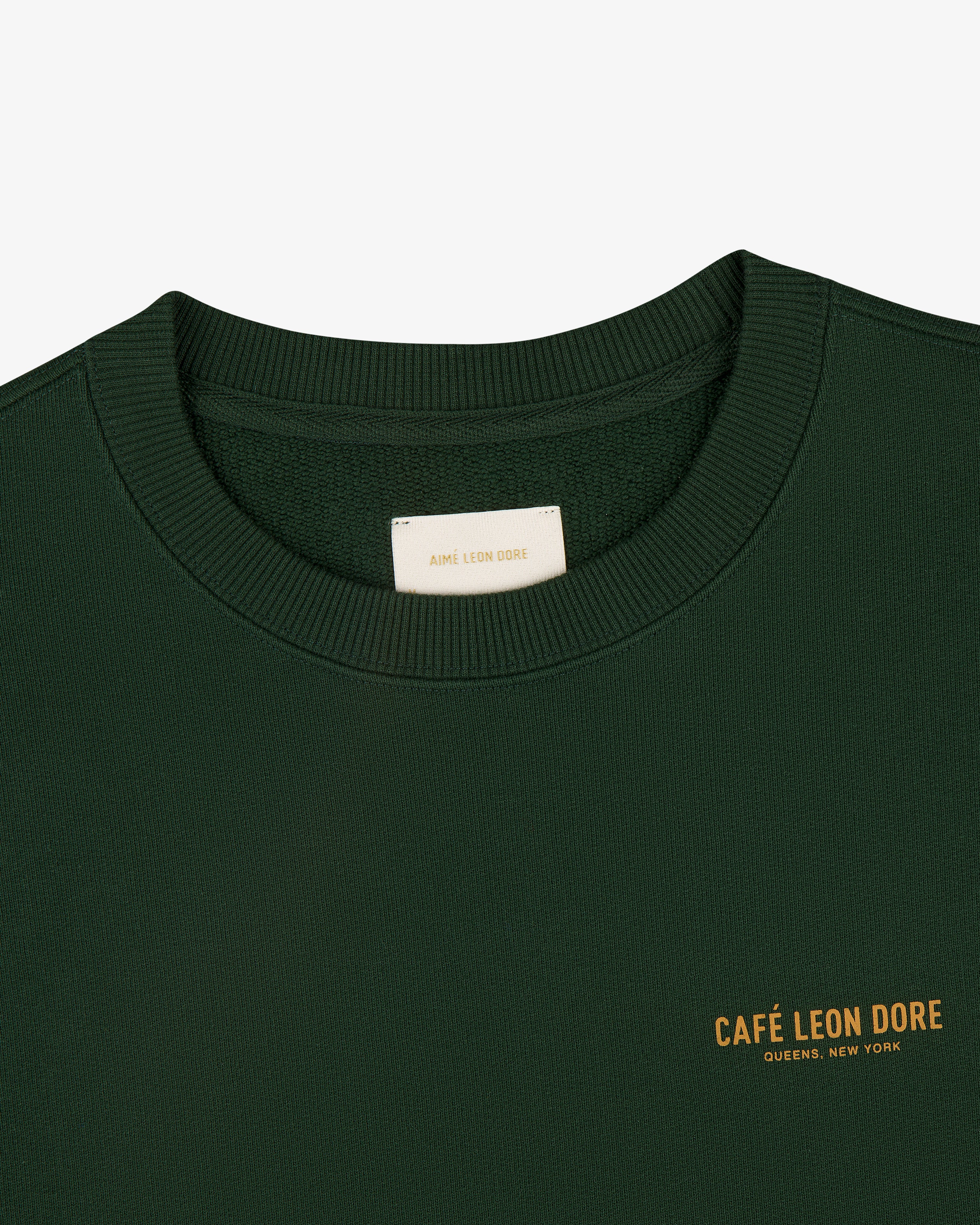 Café Leon Dore Crewneck Sweatshirt in dark green with yellow "CAFÉ LEON DORE QUEENS, NEW YORK" chest print.