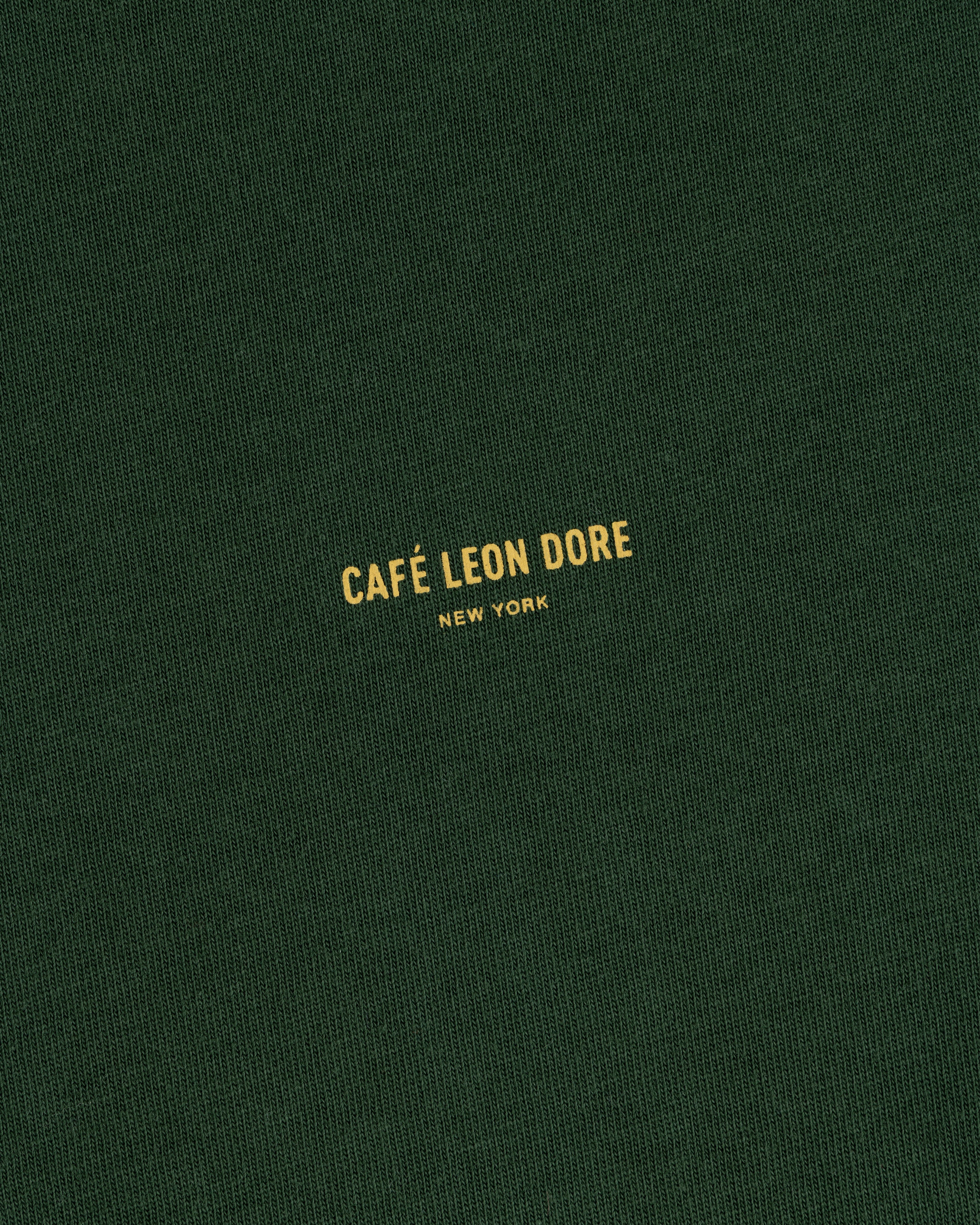Green Café Leon Dore Logo Tee with yellow “CAFÉ LEON DORE NEW YORK” text centered on the front.