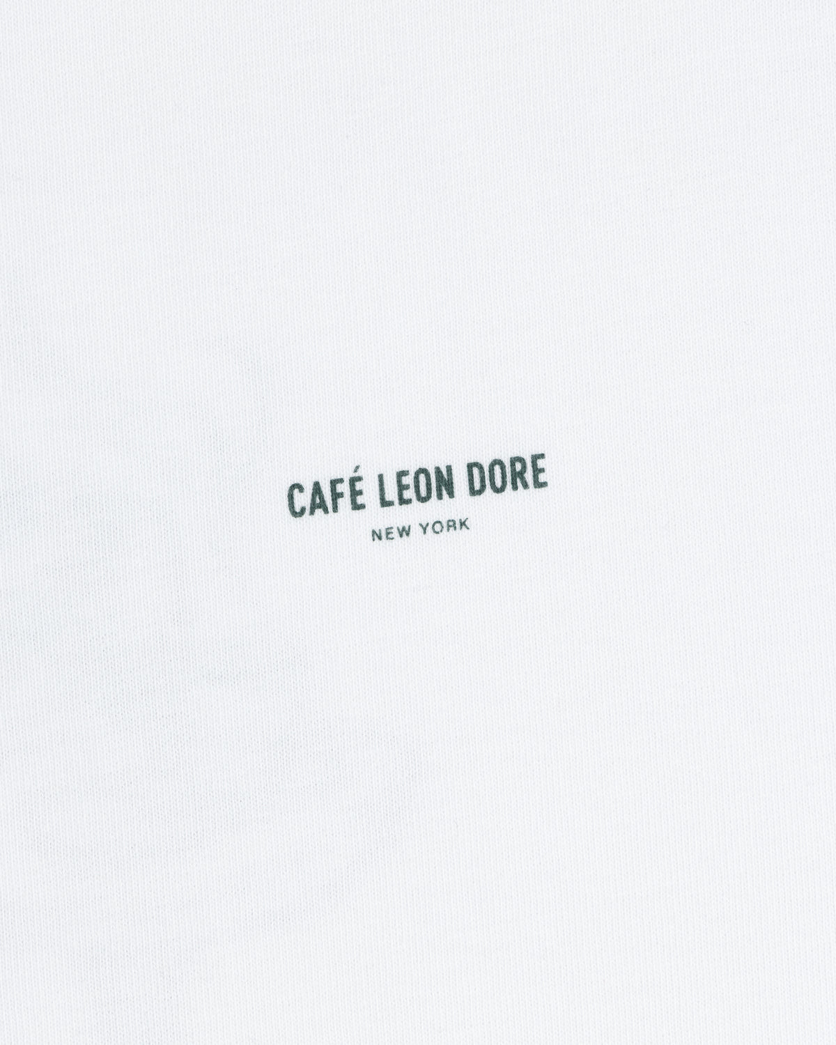 White Café Leon Dore Caricature Tee featuring small, dark “CAFÉ LEON DORE NEW YORK” print at the center.