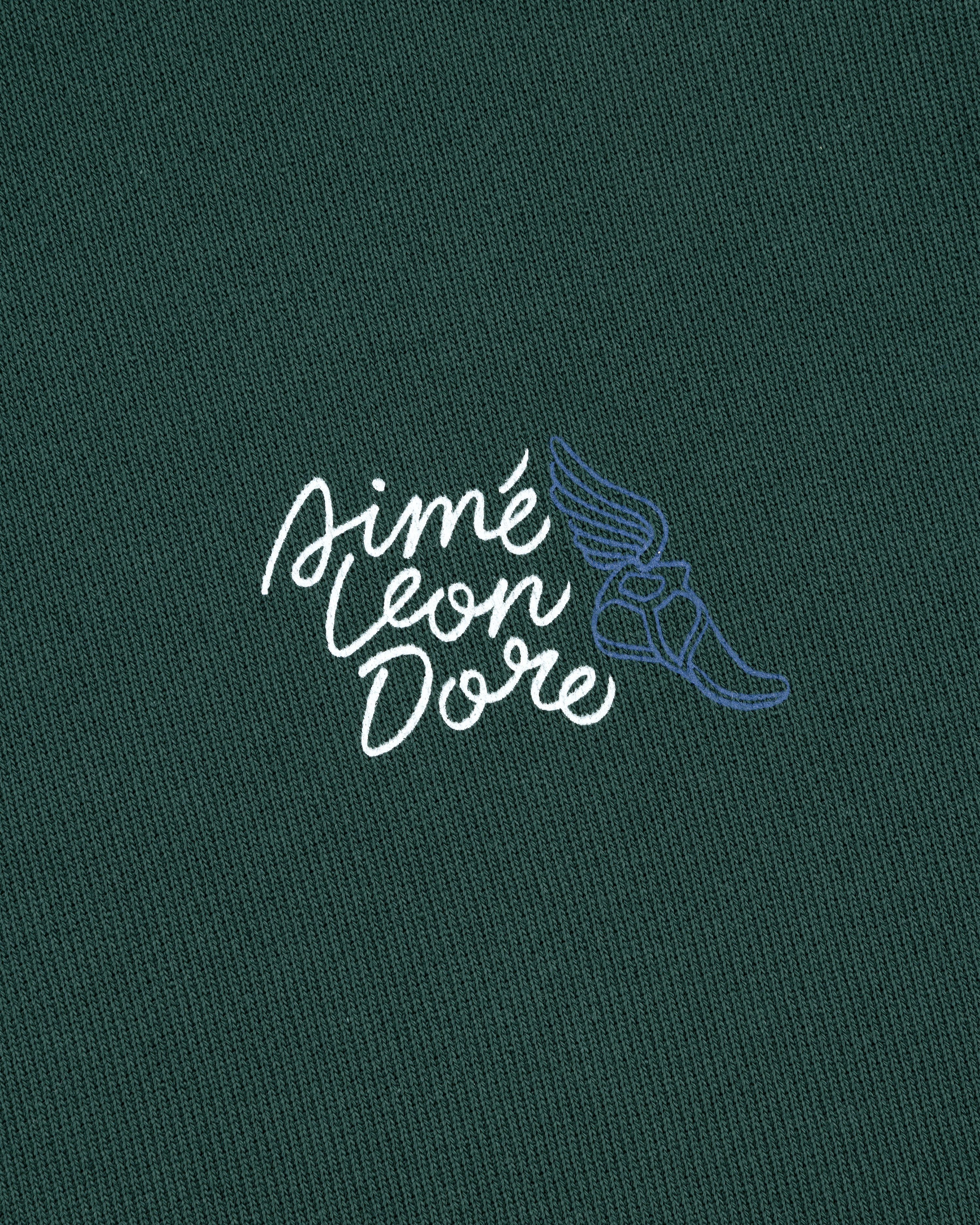 Wingfoot Track Hoodie: white Aimé Leon Dore cursive and blue winged shoe on dark green fabric.