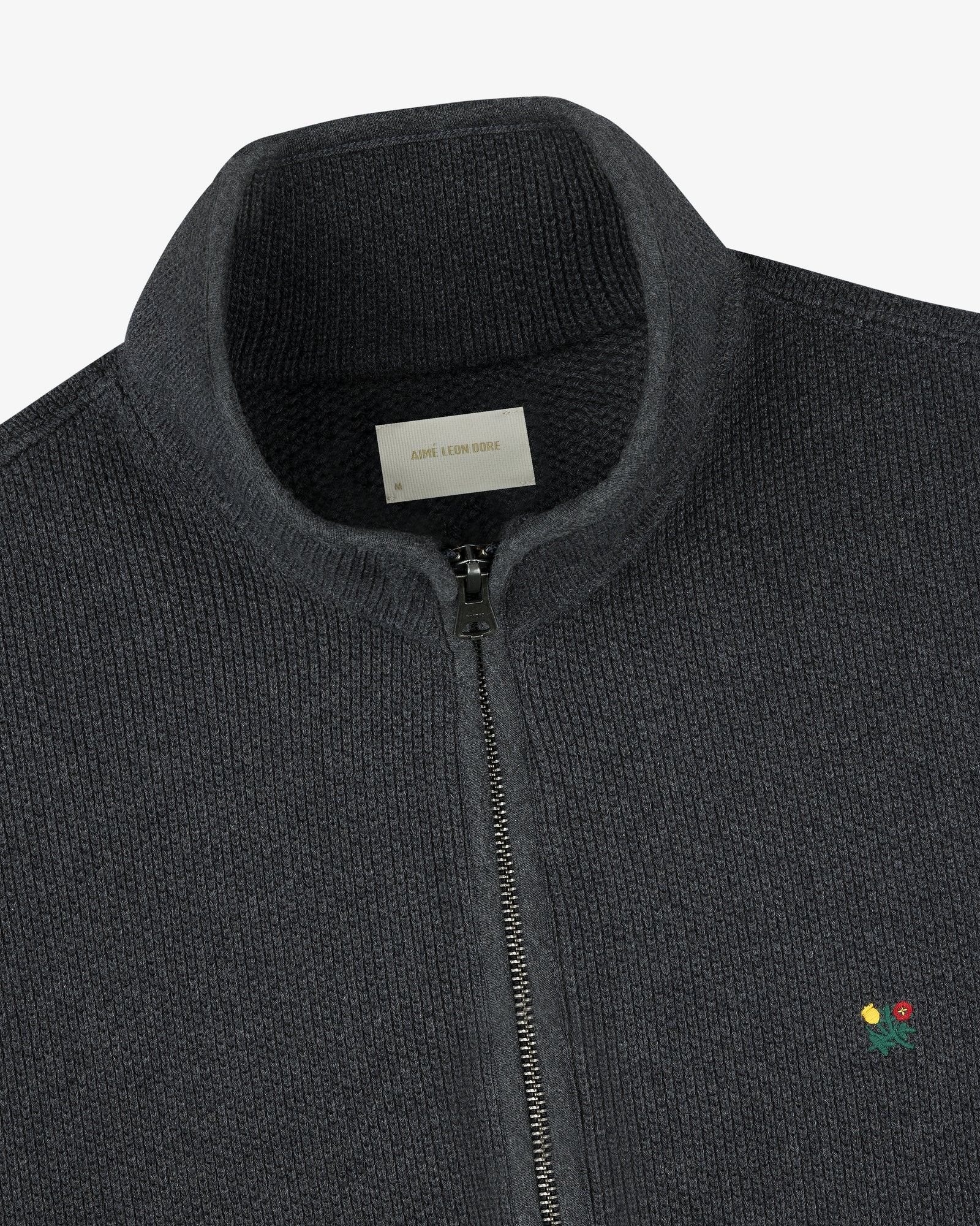 Crest Piqué Half-Zip Pullover in dark gray with ribbed texture, small embroidered flower, and visible collar label.