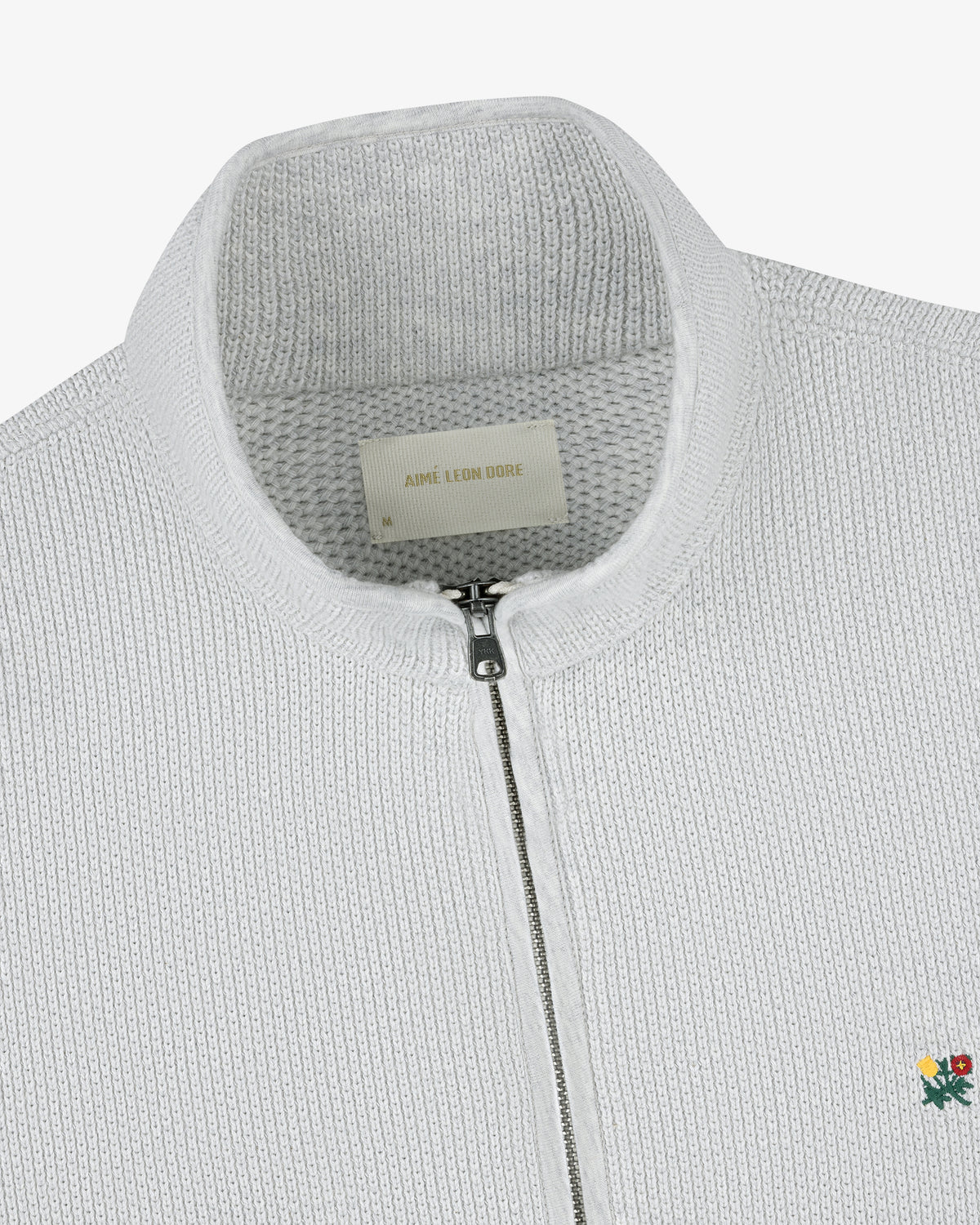 Close-up of the Crest Piqué Half-Zip Pullover, a white knit sweater with ribbed texture and embroidered flower at the hem.