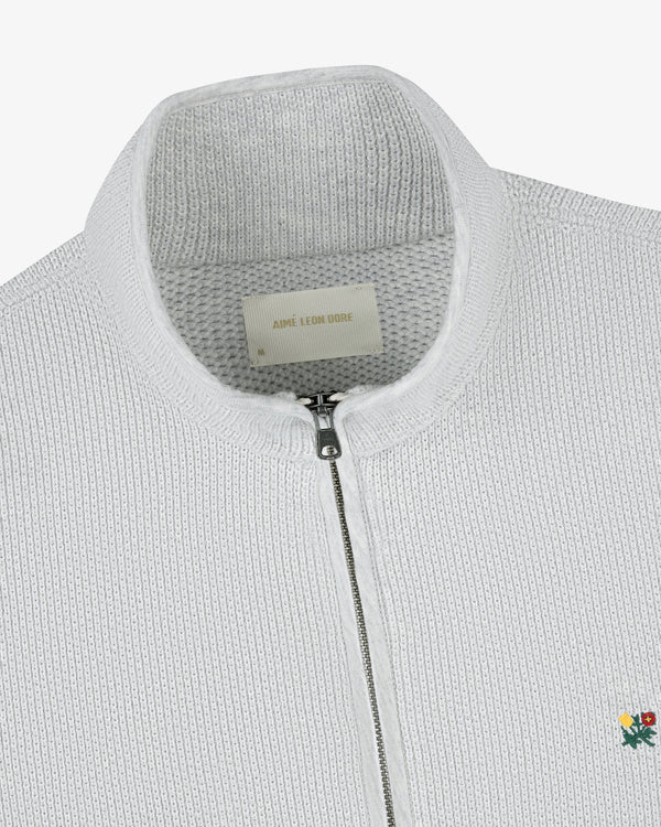 Close-up of the Crest Piqué Half-Zip Pullover, a white knit sweater with ribbed texture and embroidered flower at the hem.