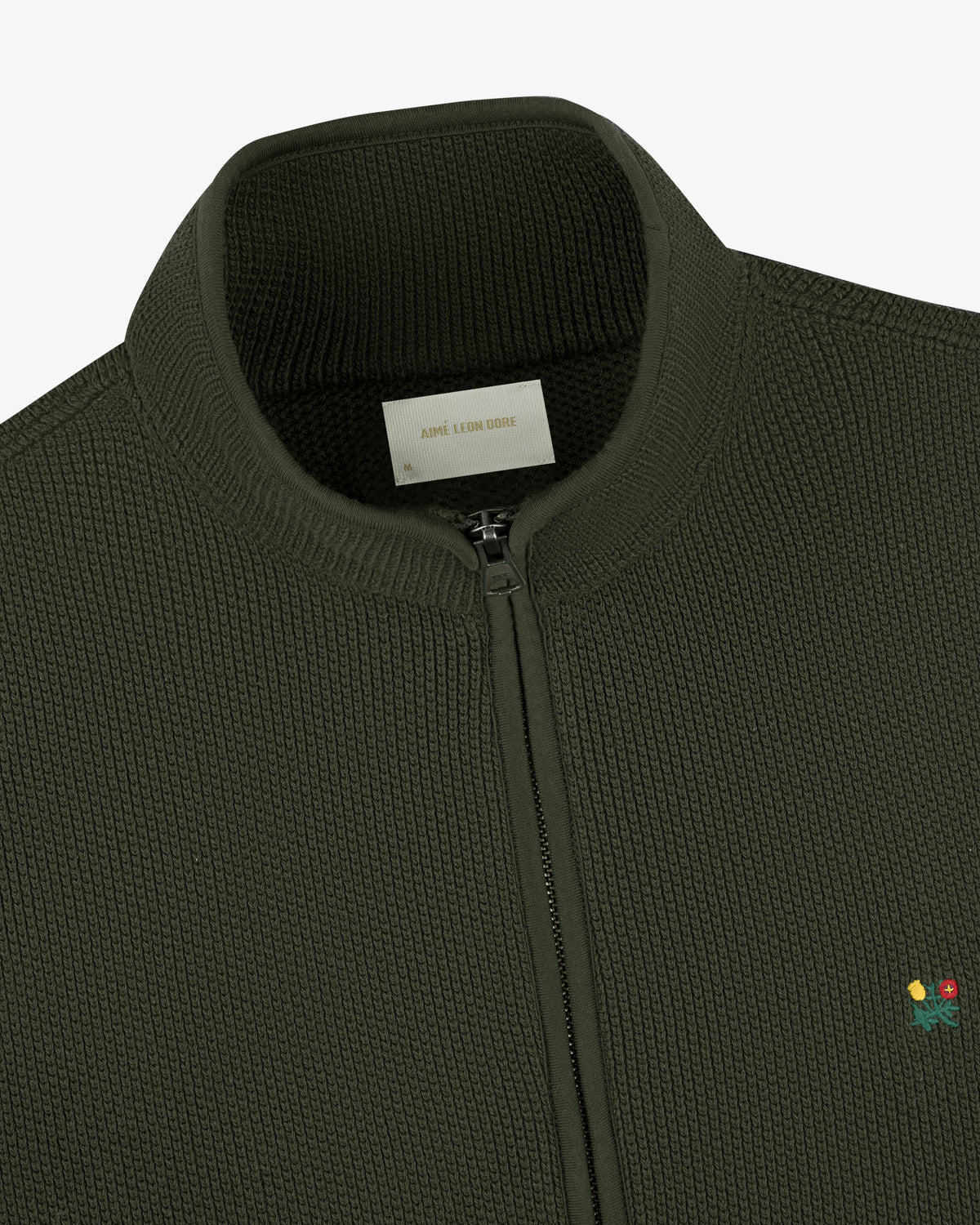 Close-up of the Crest Piqué Half-Zip Pullover in dark green with small flower embroidery and a ribbed collar.
