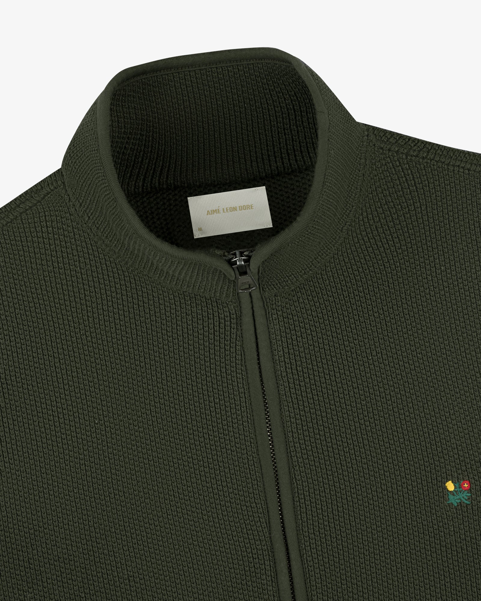 Close-up of the Crest Piqué Half-Zip Pullover in dark green with small flower embroidery and a ribbed collar.