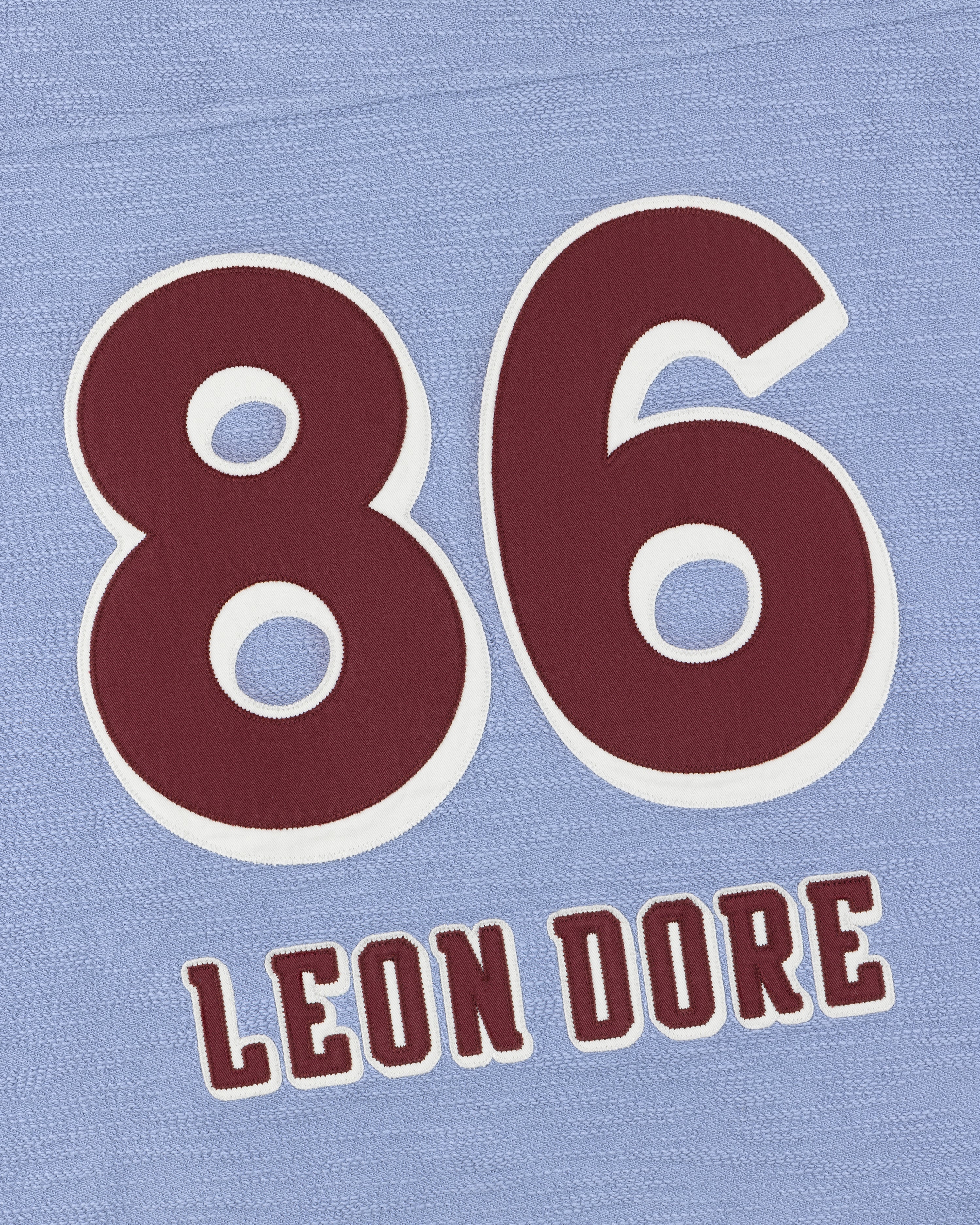 Bold red 86 with LEON DORE below, on a light blue Legacy Slub Football Jersey with textured background.