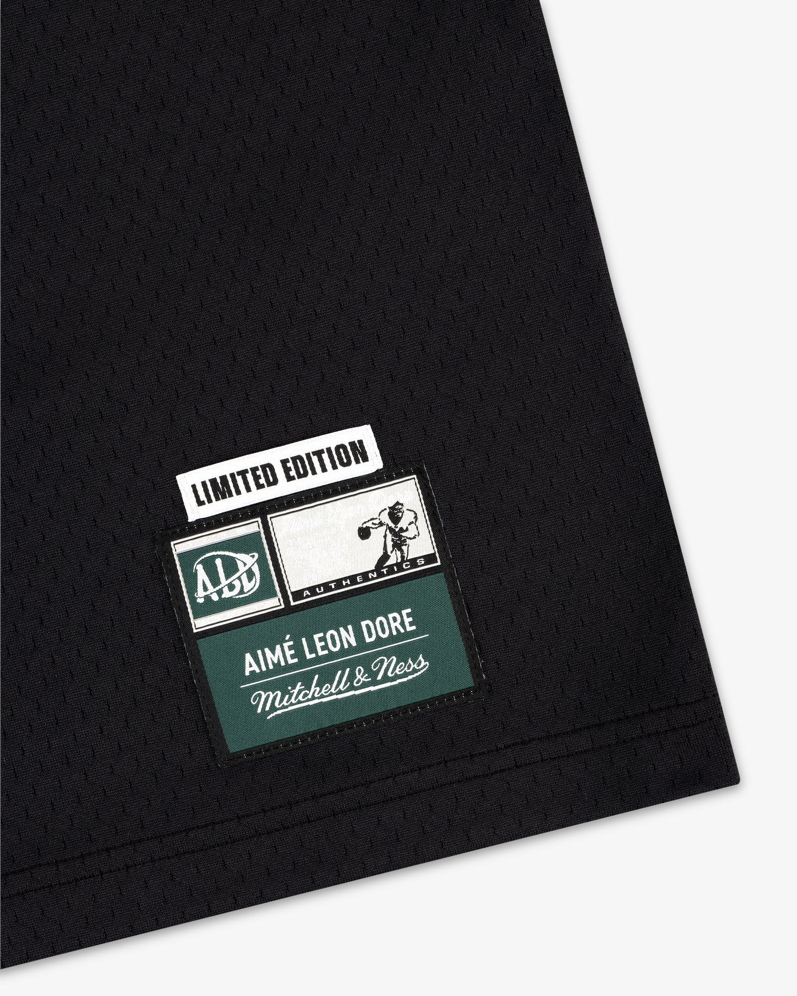 Black jersey with stitched patch: “Limited Edition Aimé Leon Dore Mitchell & Ness” and sports graphic.