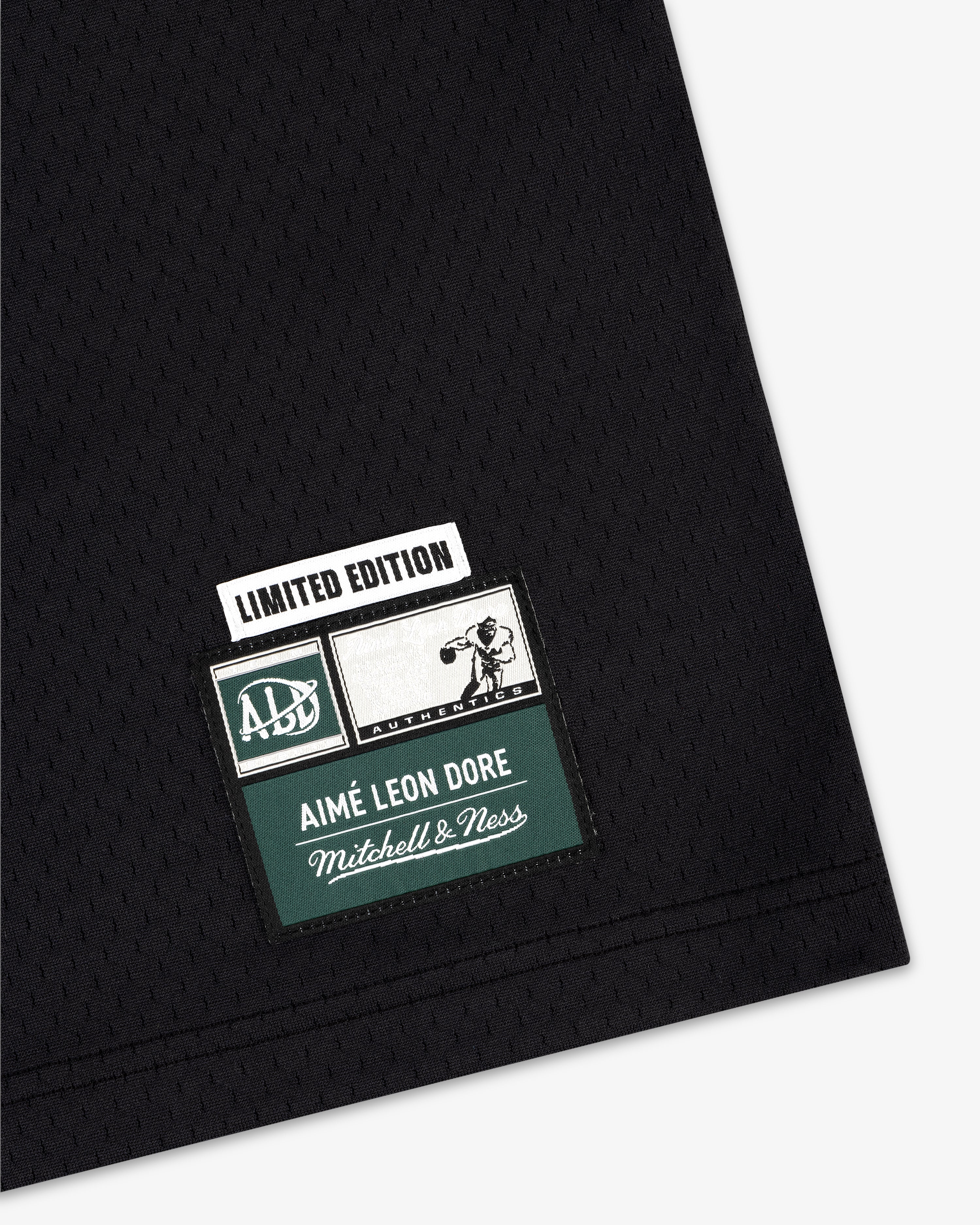 Black jersey with stitched patch: “Limited Edition Aimé Leon Dore Mitchell & Ness” and sports graphic.